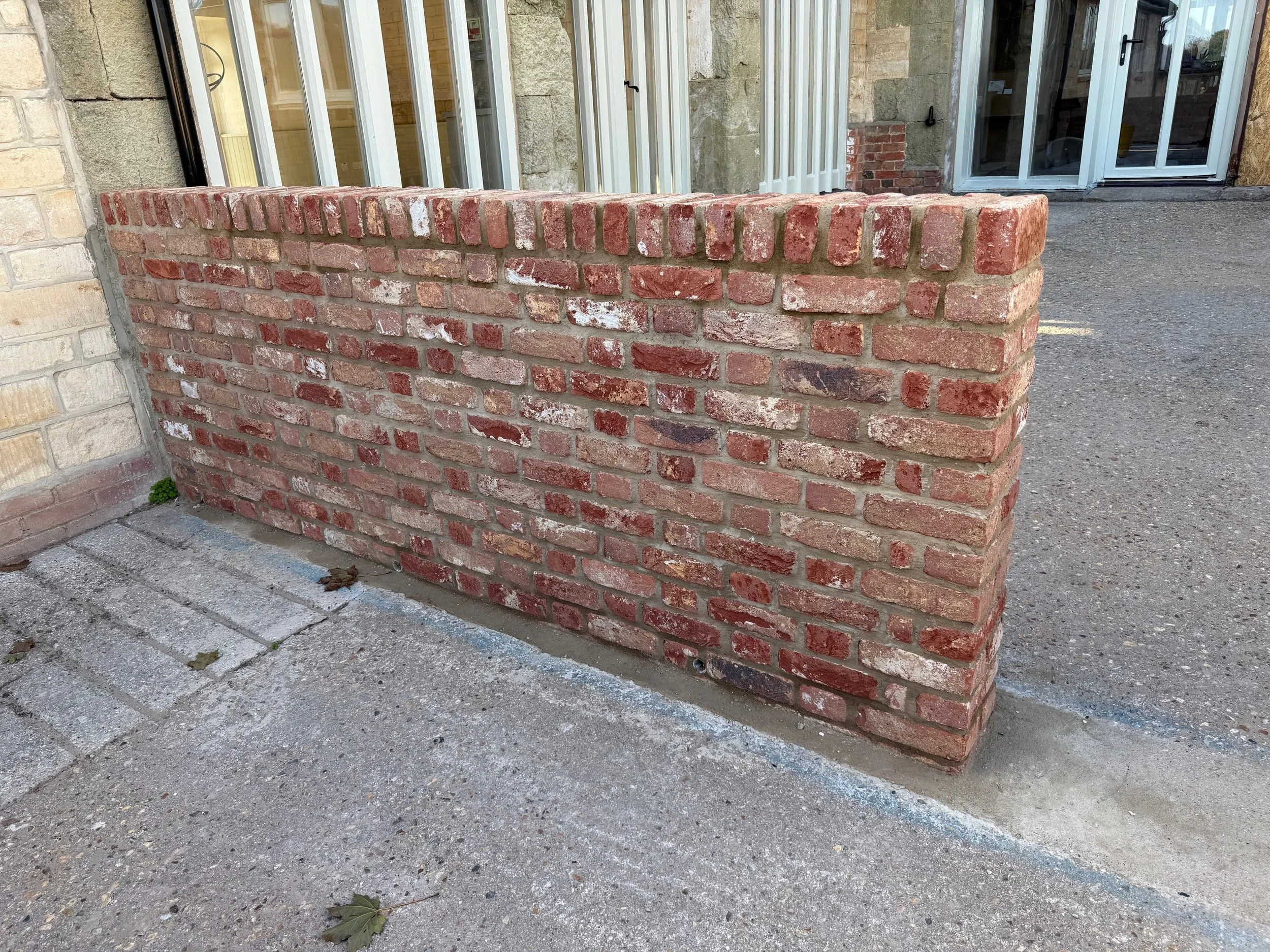 A short brick wall with a red and brown pattern in front of a building with beige and brick walls and glass doors.