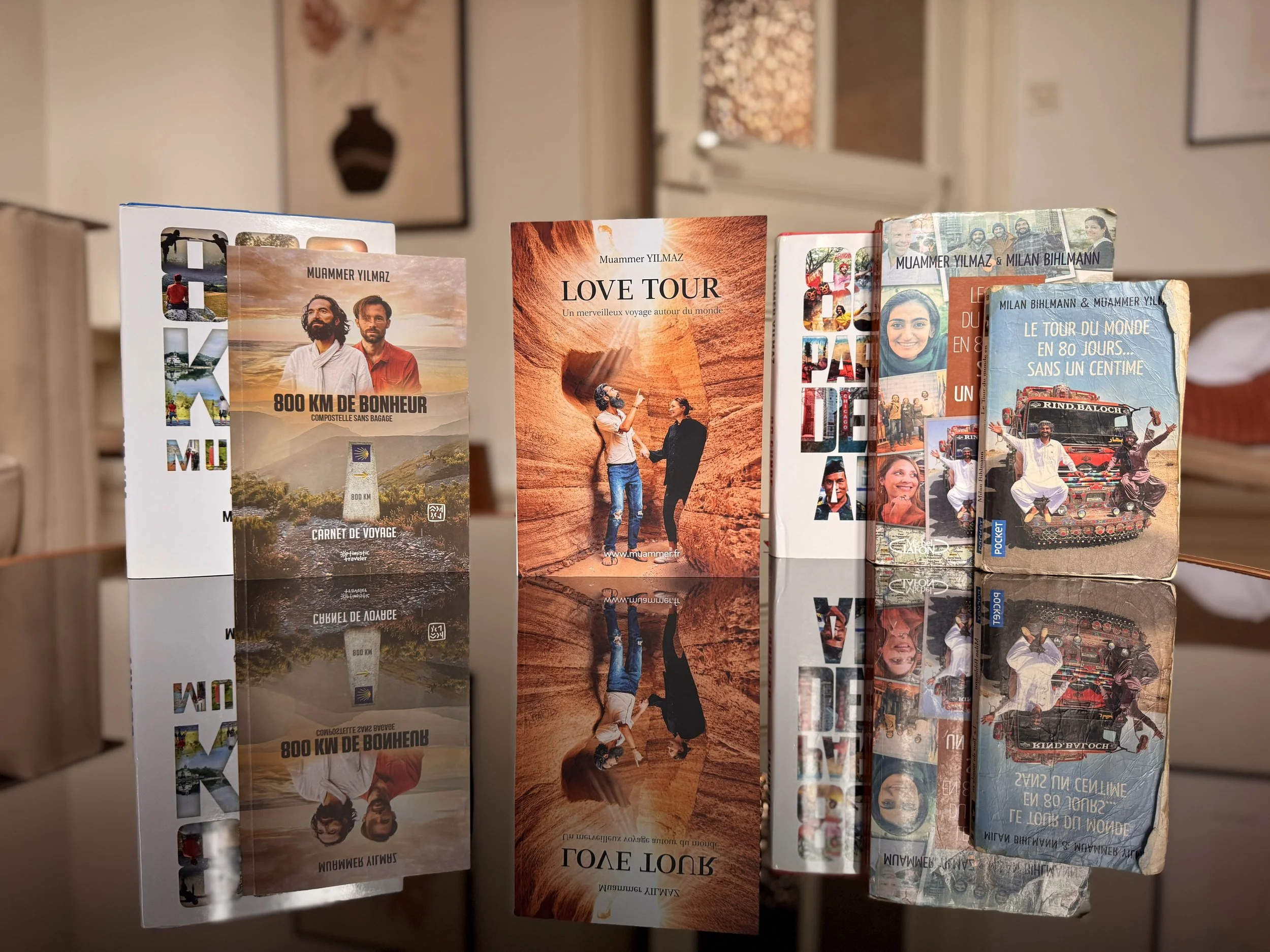 Books displayed on a reflective surface showing various travel and adventure titles, some featuring images of people and scenic landscapes.