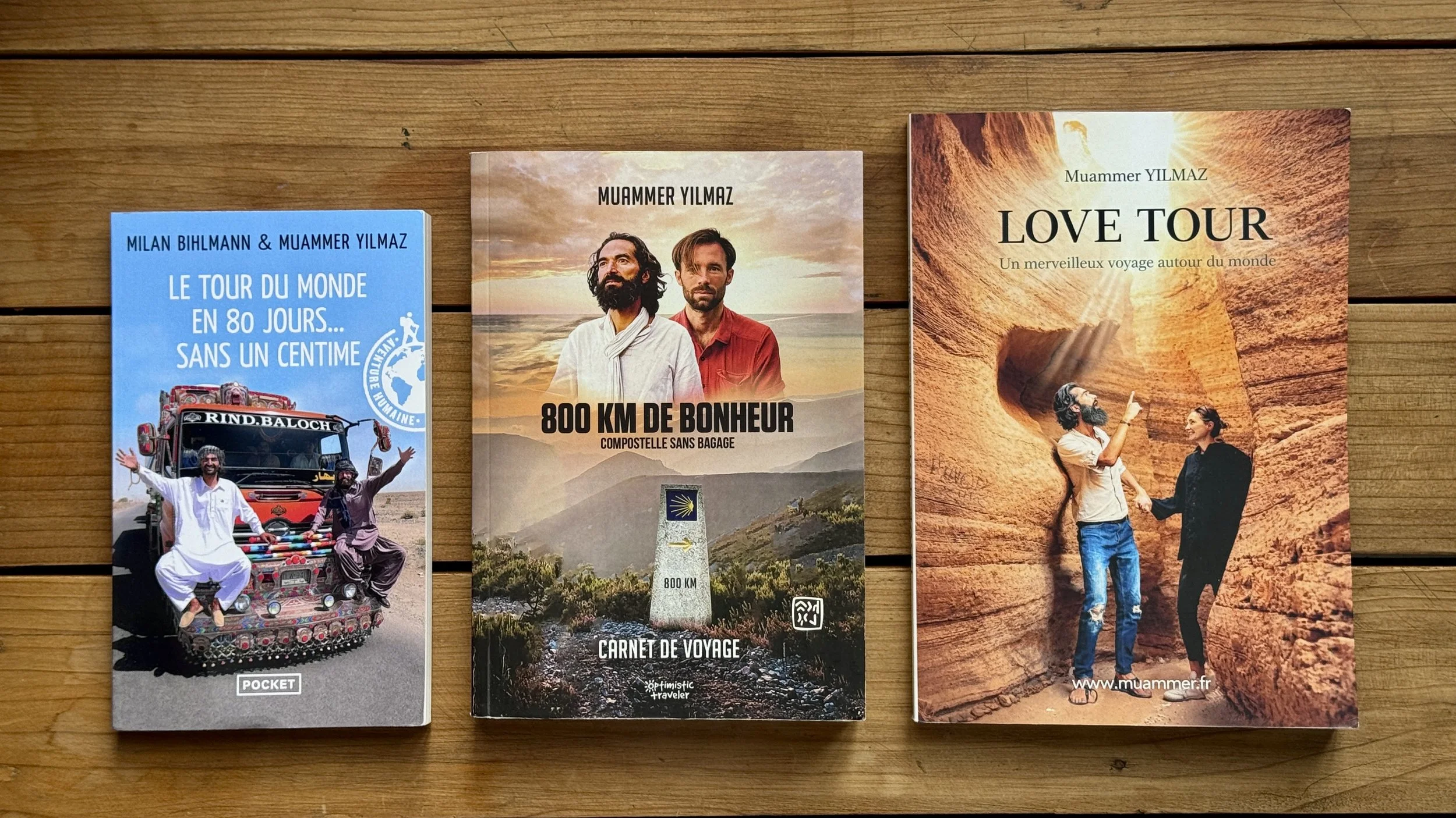 Les 3 livres de Muammer Yilmaz. Three travel books on a wooden surface, featuring titles about world travel, happiness, and nature adventures.