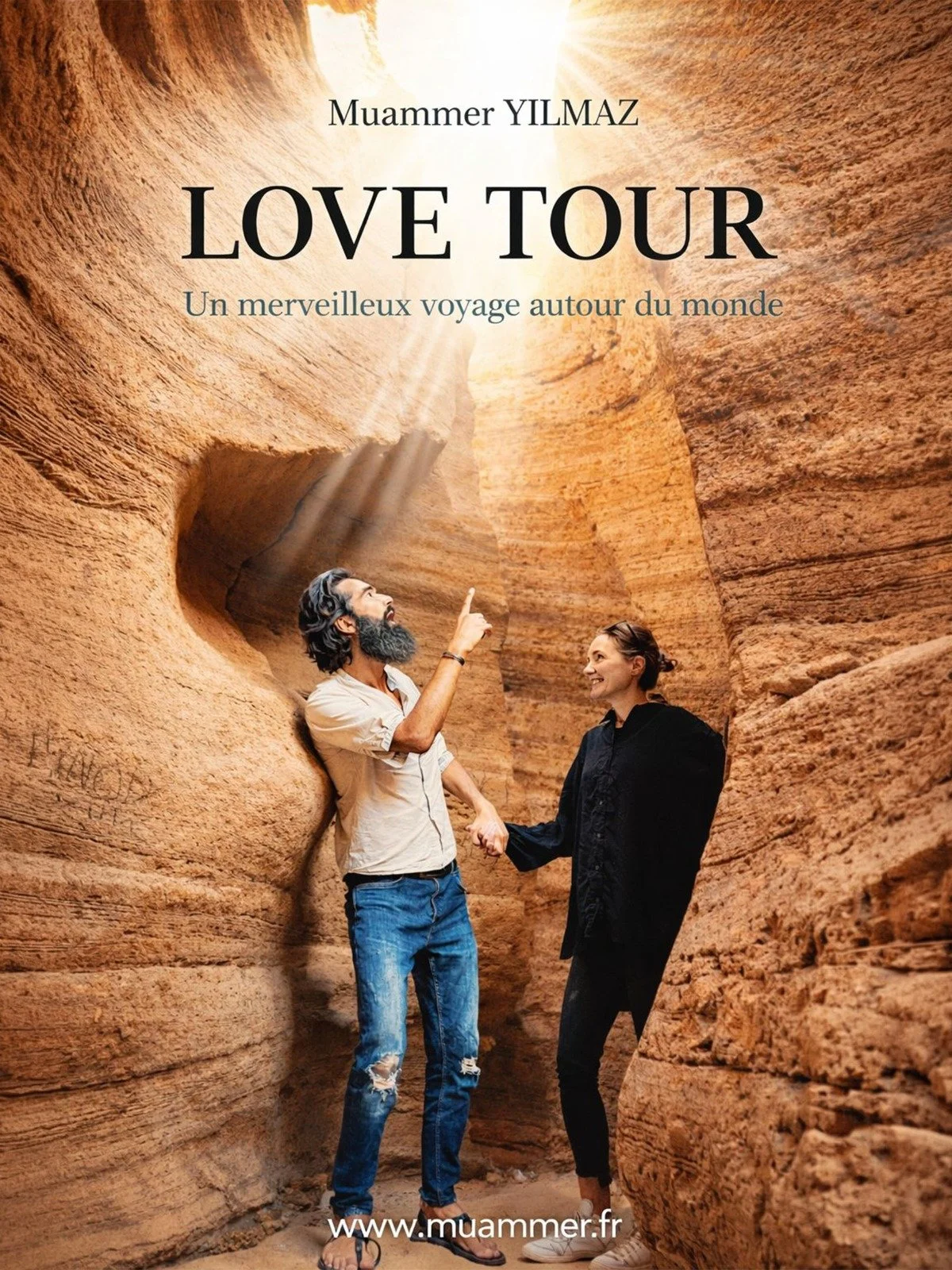 The cover of a book titled "Love Tour" by Muammer Yilmaz features a man and a woman holding hands inside a canyon with towering rocky walls. The man has a beard, long hair, and wears casual clothes, while the woman is smiling and dressed in black. Sunlight shines through the top opening of the canyon, illuminating the scene. The website www.muammer.fr is displayed at the bottom.