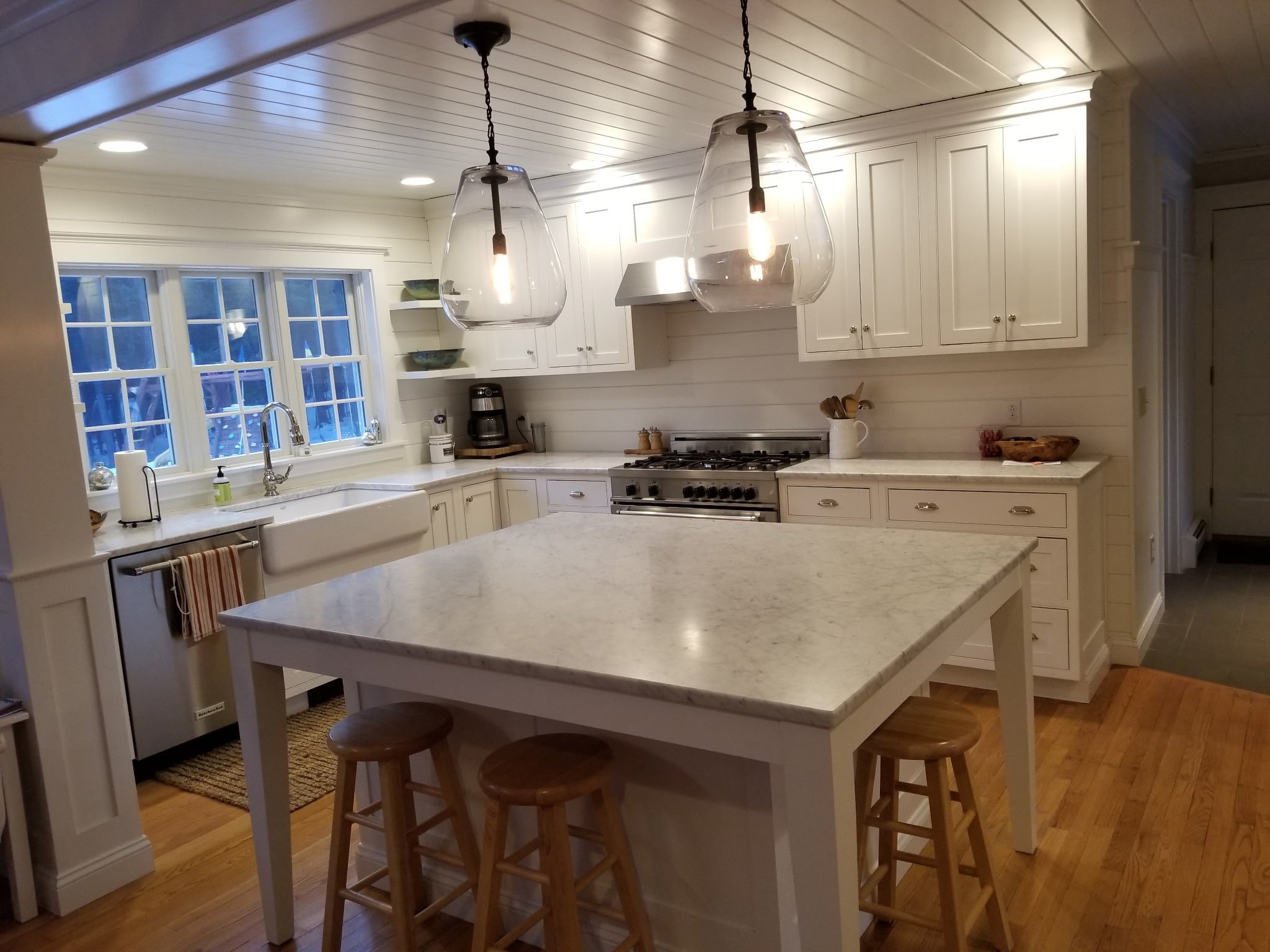 Bright white kitchen with large window, white cabinets, a marble island, and pendant lights.