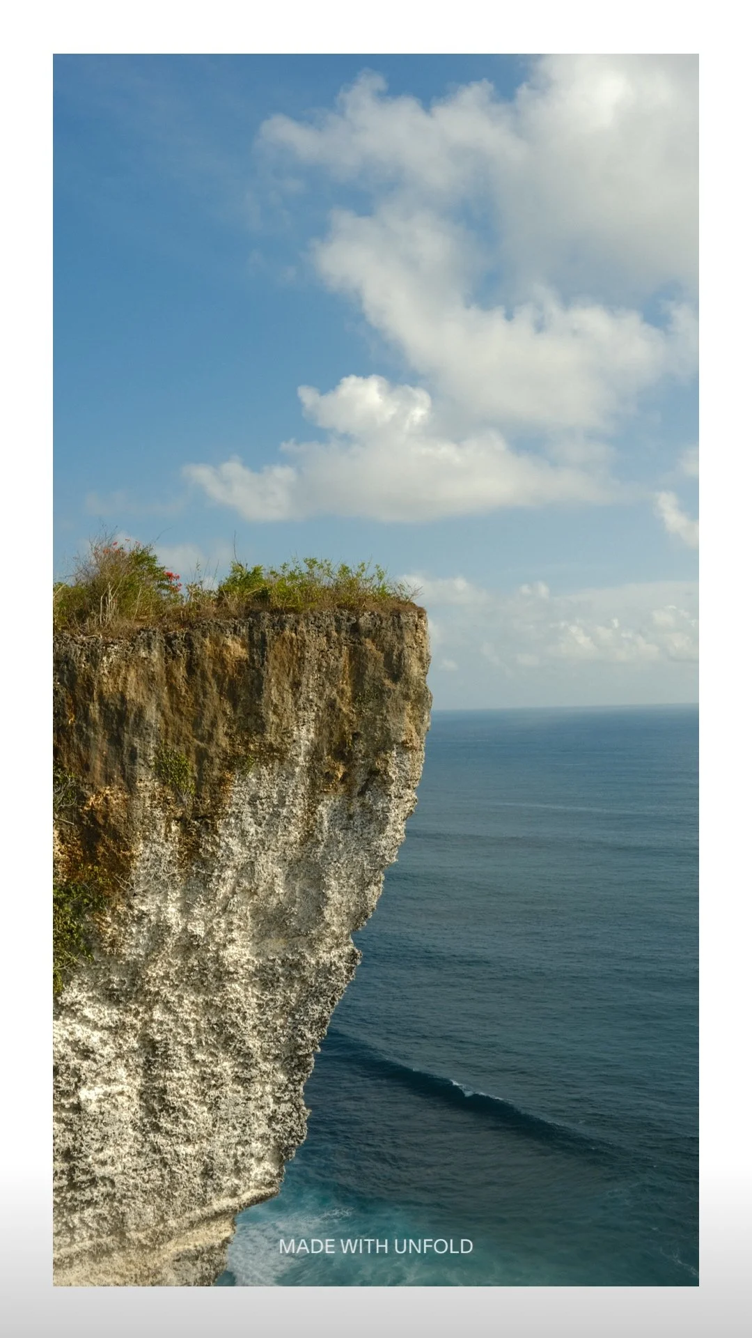 Cliffside overlooking the ocean with blue sky and scattered clouds.