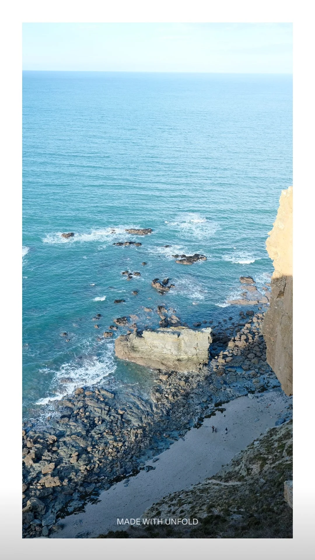 Scenic view of the ocean from a rocky cliff with a small sandy beach below, clear blue sky
