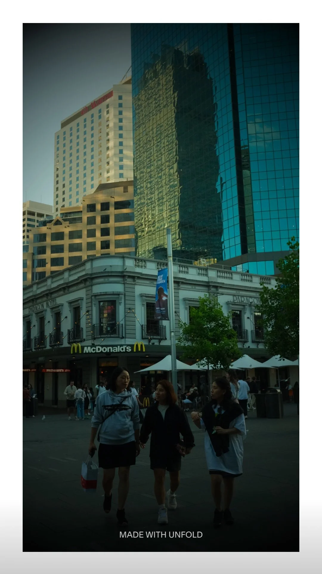 People walking in a city street with tall modern buildings and a McDonald's restaurant in the background.
