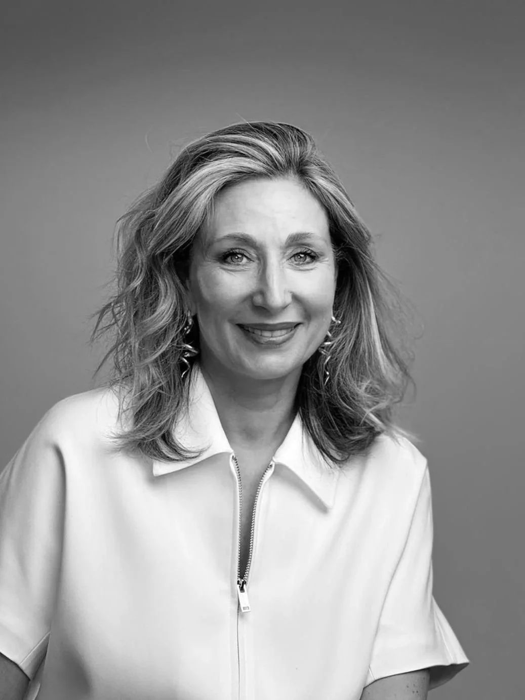 Portrait en noir et blanc d'une femme souriante avec des cheveux bouclés, portant une veste à zip.