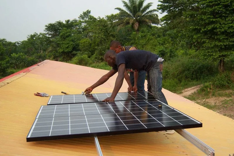 Two men installing solar panels in Africa on a yellow metal roof
