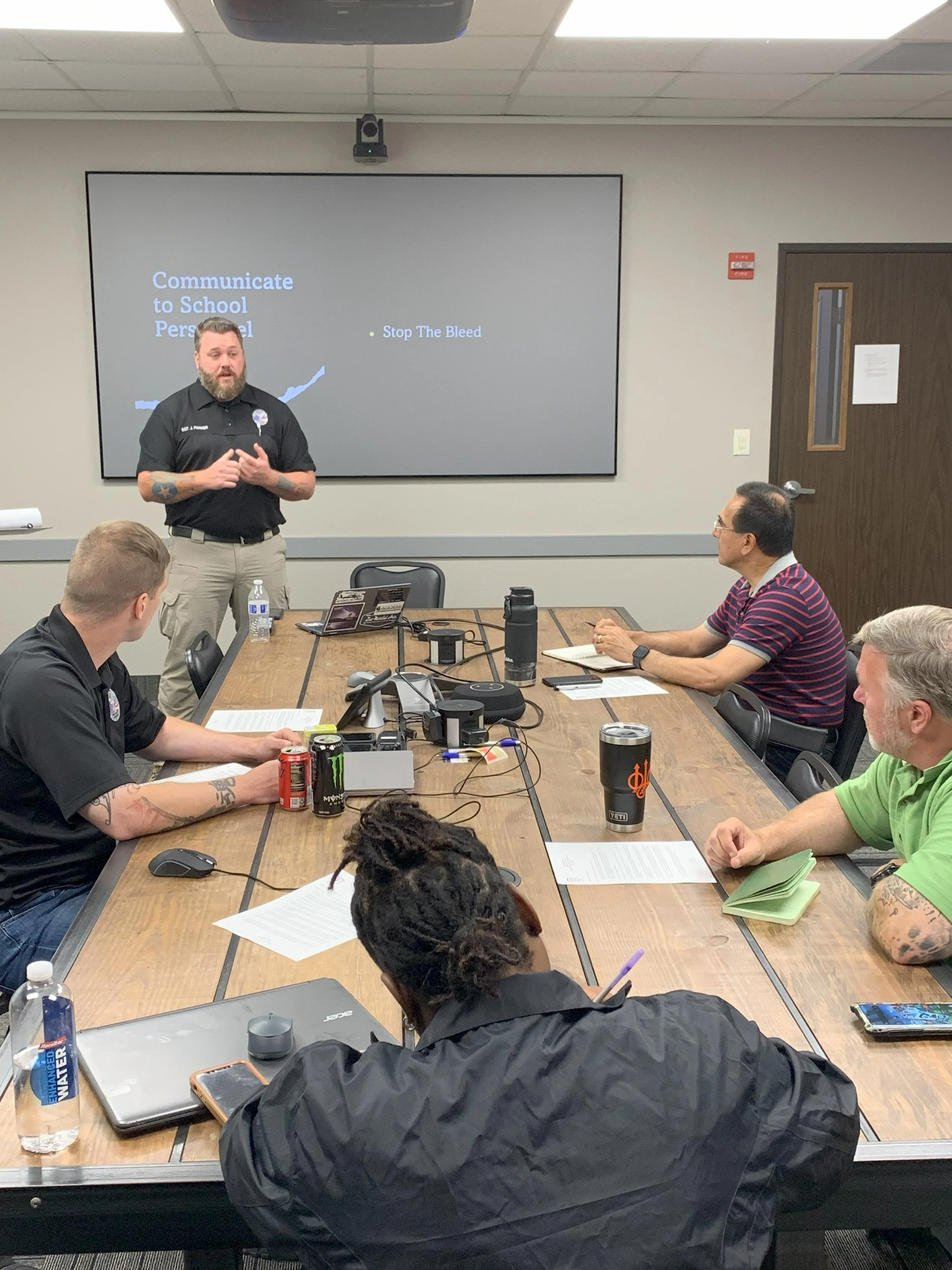A man giving a presentation about communicating with school personnel, with several people seated around a conference table listening.