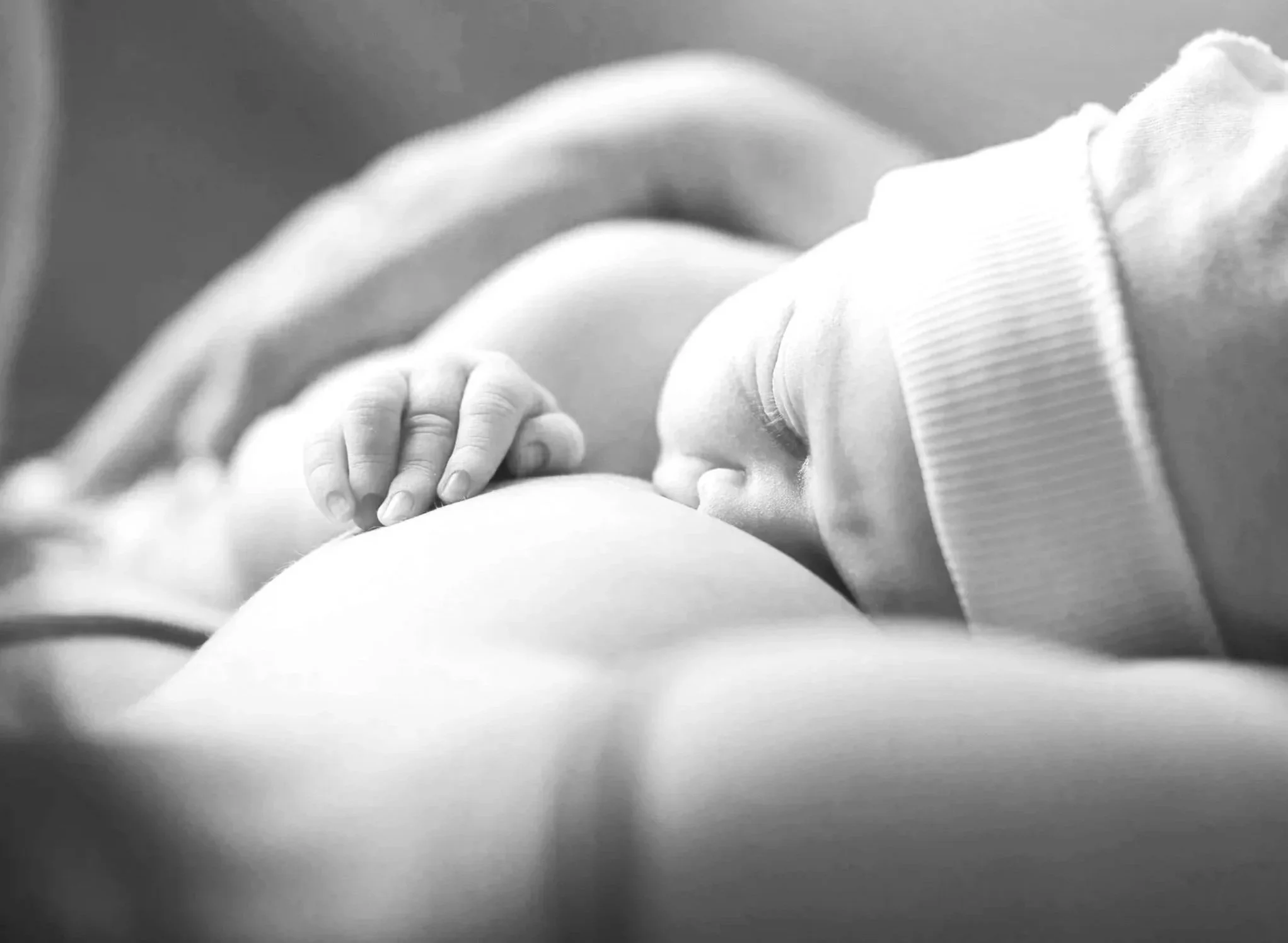 A newborn baby nursing from a mother's breast, lying on her side, in a close-up black and white photograph.
