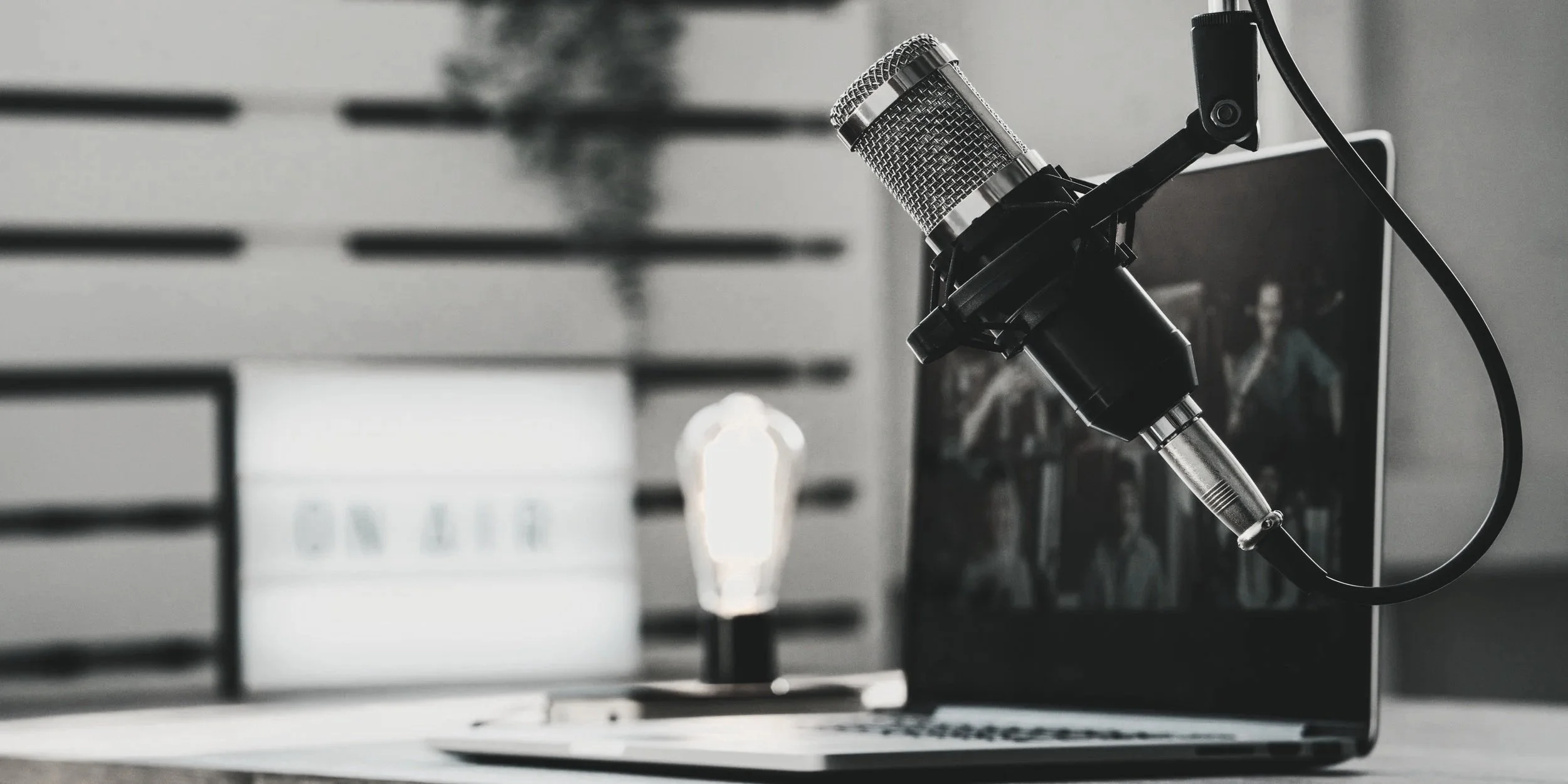 Close-up of a microphone attached to a laptop, with a blurred computer screen and a background image of a group of people.