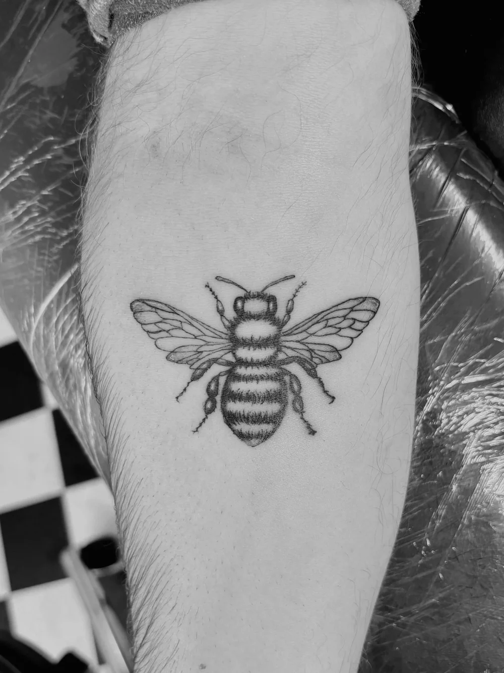 Detailed bee tattoo on a forearm with whip and stipple shading