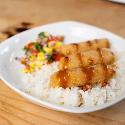 Fried fish strips on rice with a side of colorful diced vegetable salad on a white plate.