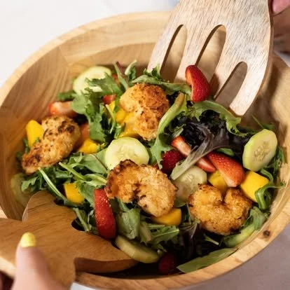 Mixed green salad with strawberries, cucumber slices, and fried chicken pieces in a wooden bowl.