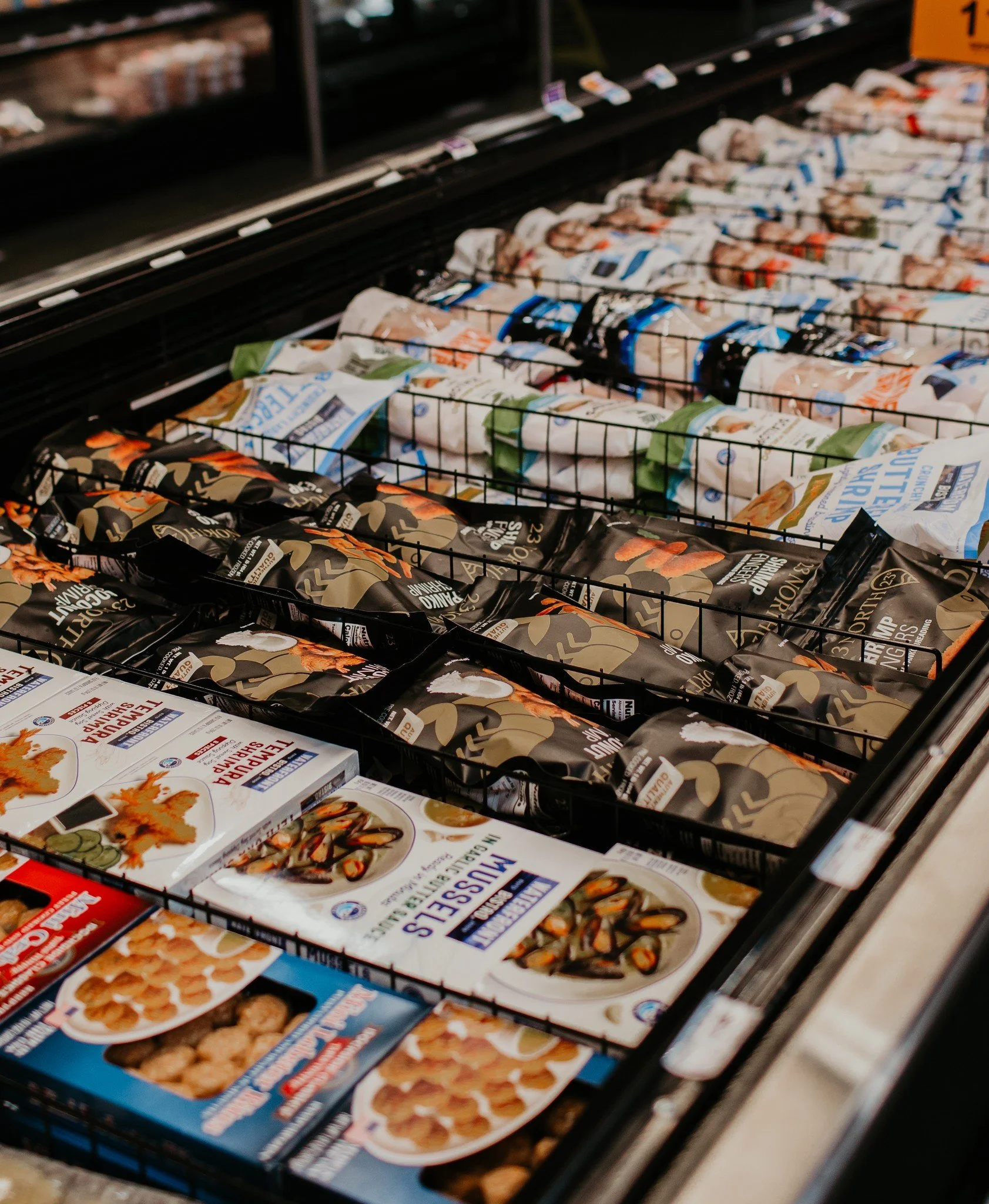 Frozen seafood and food packages in a grocery store freezer, including mussels, fish nuggets, and crab cakes.