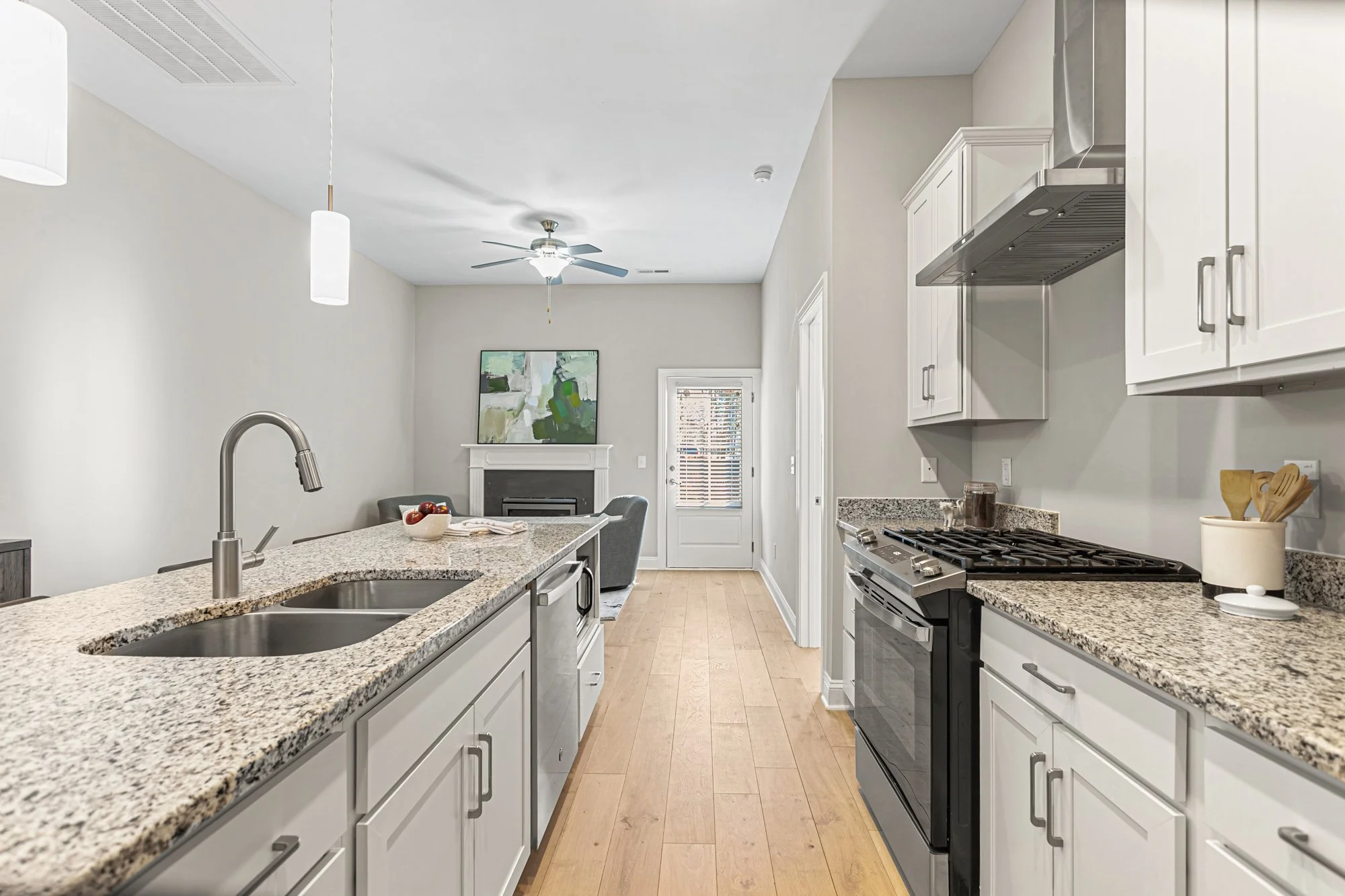 Modern kitchen with granite countertops, white cabinets, stainless steel appliances, and a view of a living room with a fireplace and a patio door.