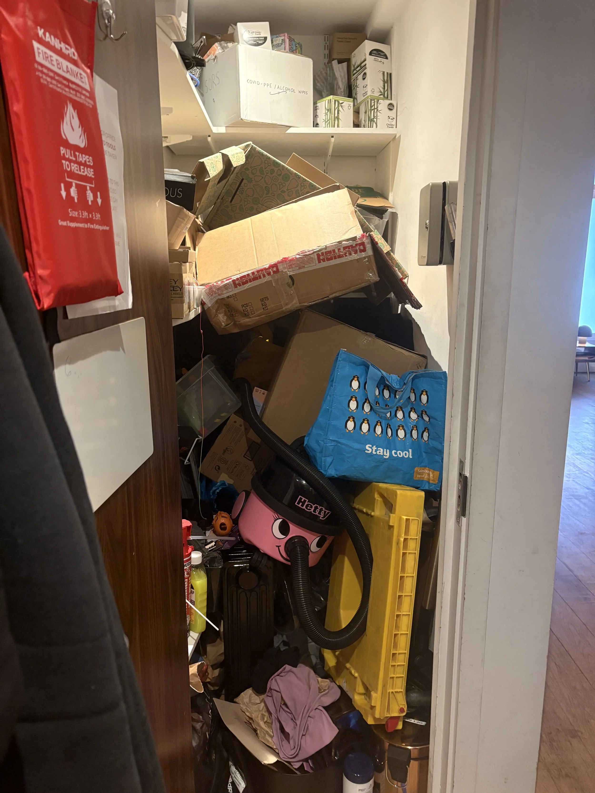 Cluttered storage closet filled with boxes, cleaning supplies, and miscellaneous household items.