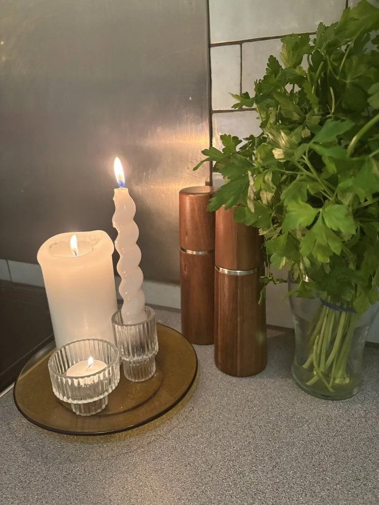 Decorative candles and a vase of green parsley on a kitchen countertop.