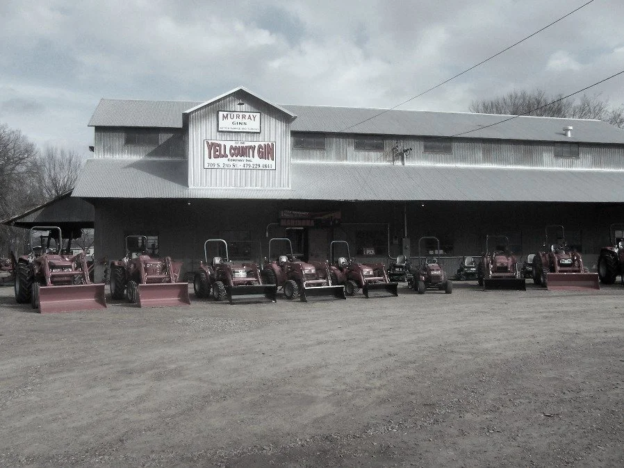 Exterior of Yell County Gin, a retired cotton gin with a sign reading 'Yell County Gin,' with several tractors parked in front.
