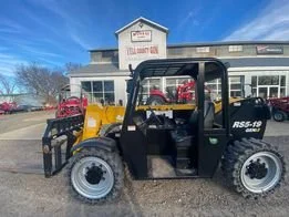 A compact utility vehicle parked in front of a building with a sign that reads 'Tire Shop.' The vehicle is black and yellow with a roll cage and large tires. Located at Yell county gin co. 