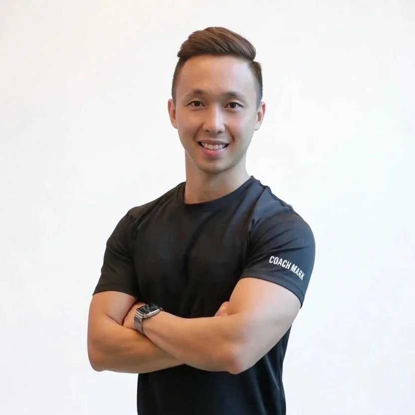 A smiling young man with short brown hair, wearing a black athletic t-shirt with white text on the sleeve that reads "COACH MARL". He is standing against a plain white background with arms crossed.