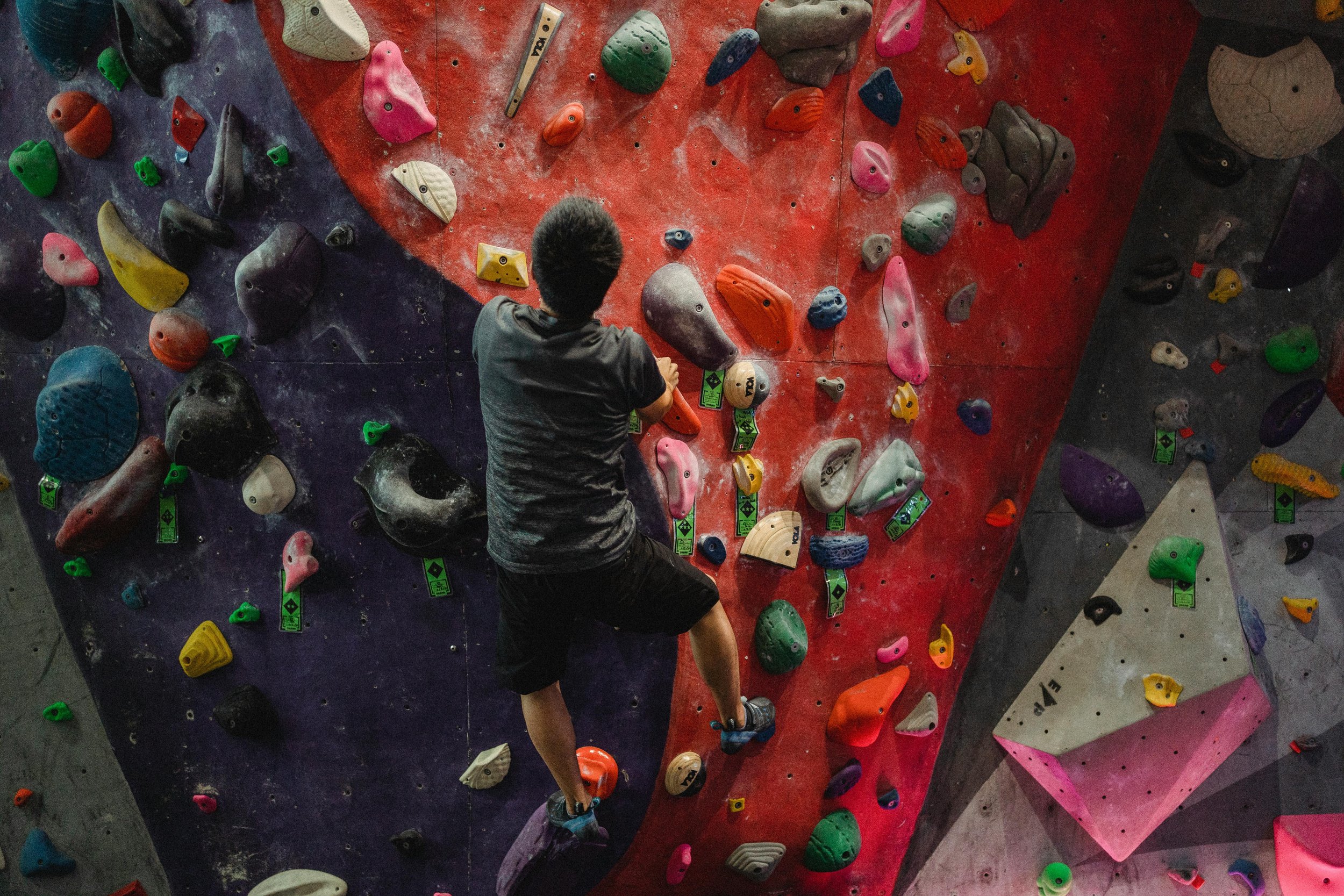 A person bouldering on an indoor climbing wall with colorful handholds and footholds.