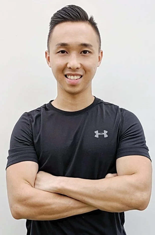 A young man with short black hair smiling, wearing a black Under Armour t-shirt, standing against a plain white background.