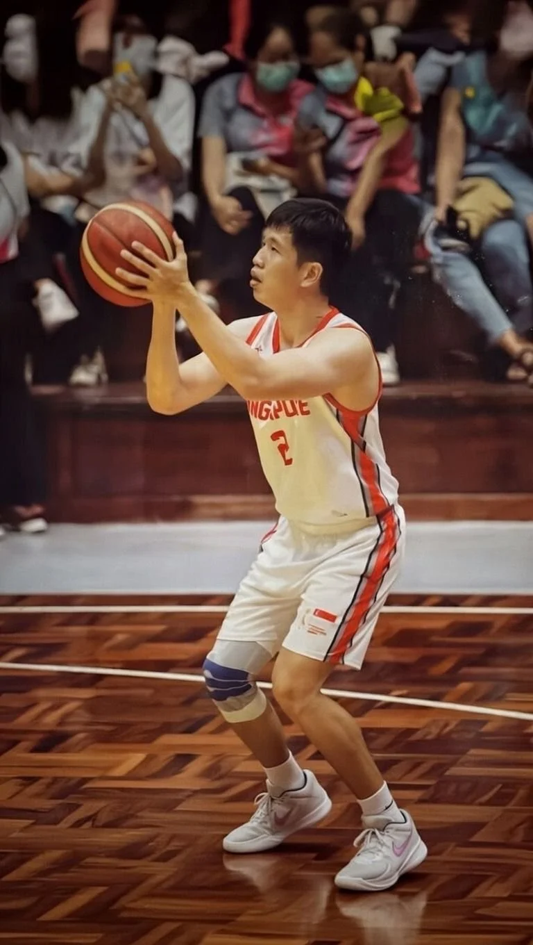 A young male basketball player wearing a white jersey with red accents and the number 2, preparing to shoot a basketball on a polished wooden court with an audience in the background.
