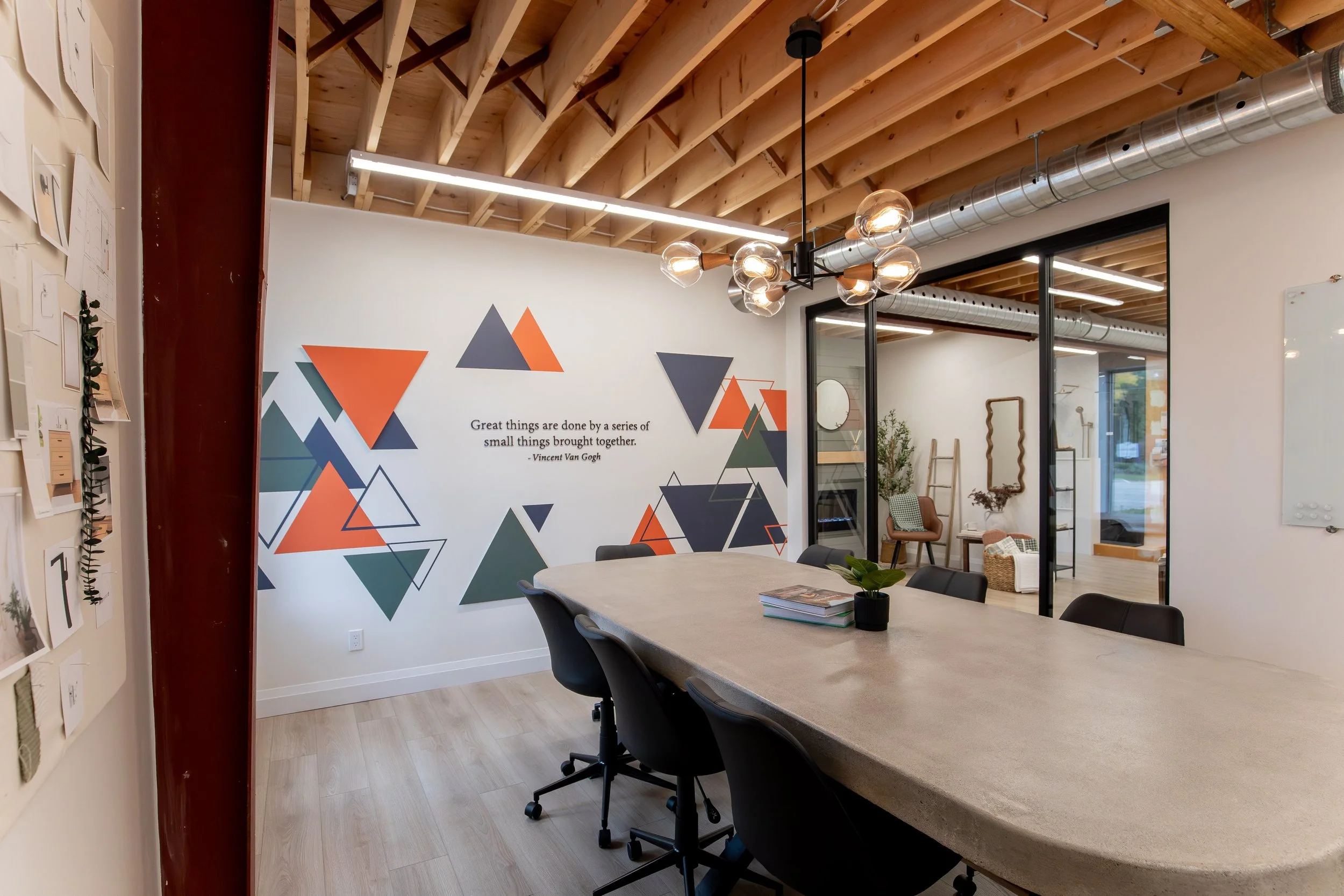 Modern conference room with a large table, black chairs, geometric wall art, quote, and adjacent seating area with lounge chairs and decor.