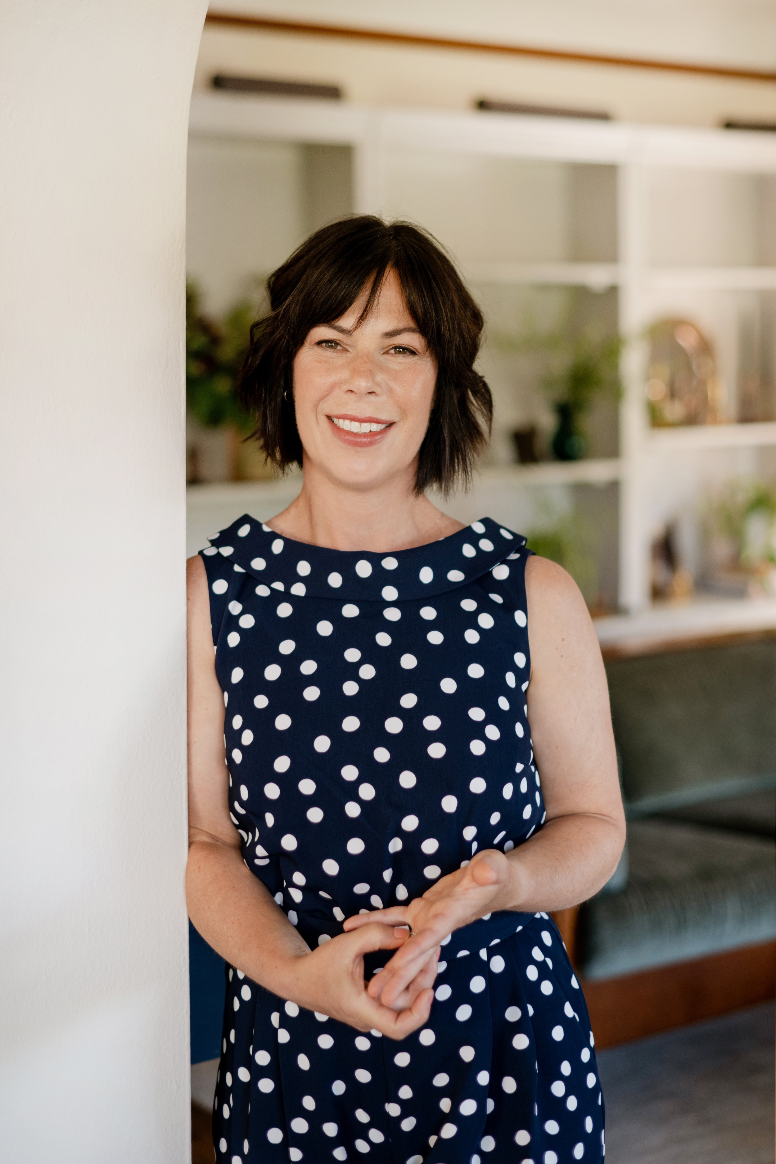 A photo of Rebecca Letwin, owner and principal designer of Full Bloom Interior Design, standing in a professionally designed living room, smiling at the camera.