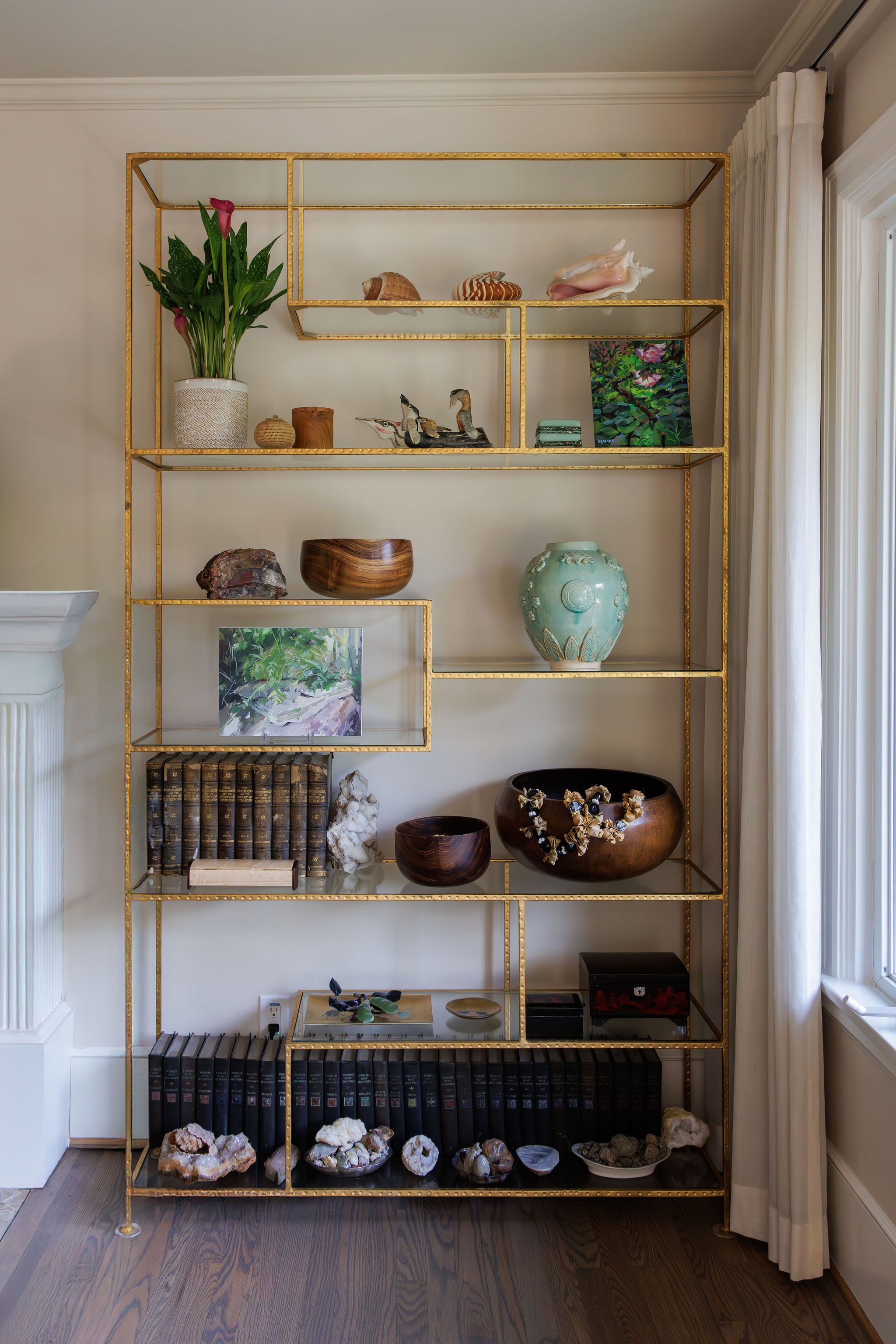 Close-up of a gold leaf etagere styled with vintage books, coastal shells, greenery and decor by Full Bloom Interior Design in Seattle.
