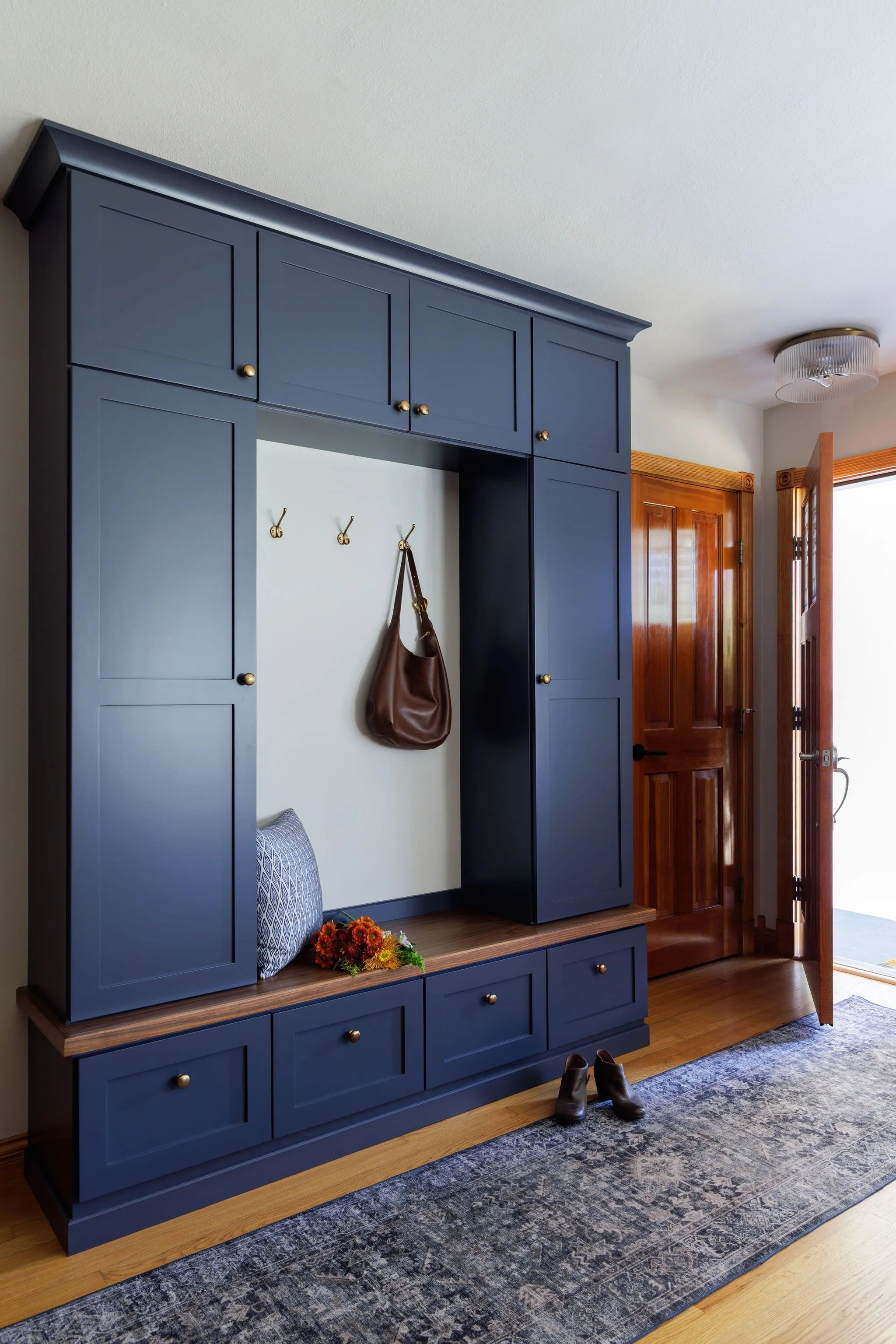 Custom navy blue entryway built-ins with gold hardware and a wood bench seat designed by Full Bloom Interior Design in Seattle.