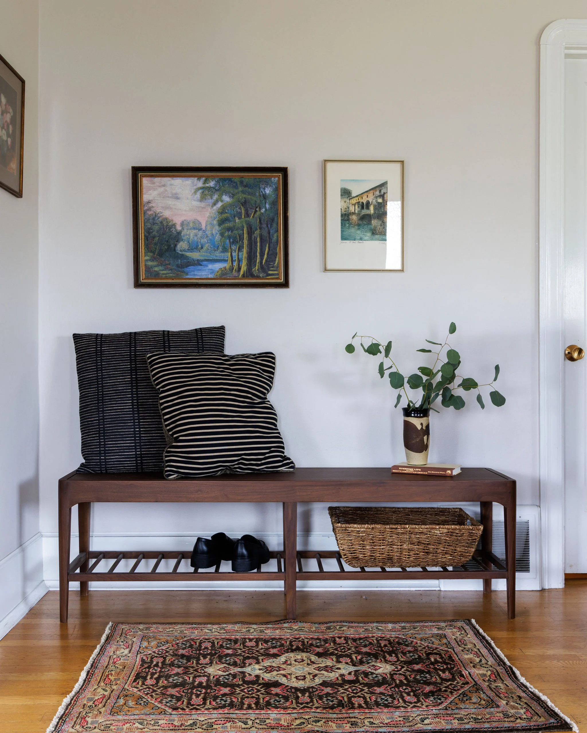Entryway with wooden bench, pillows, wall art, and vintage rug by Full Bloom Interior Design in Seattle.