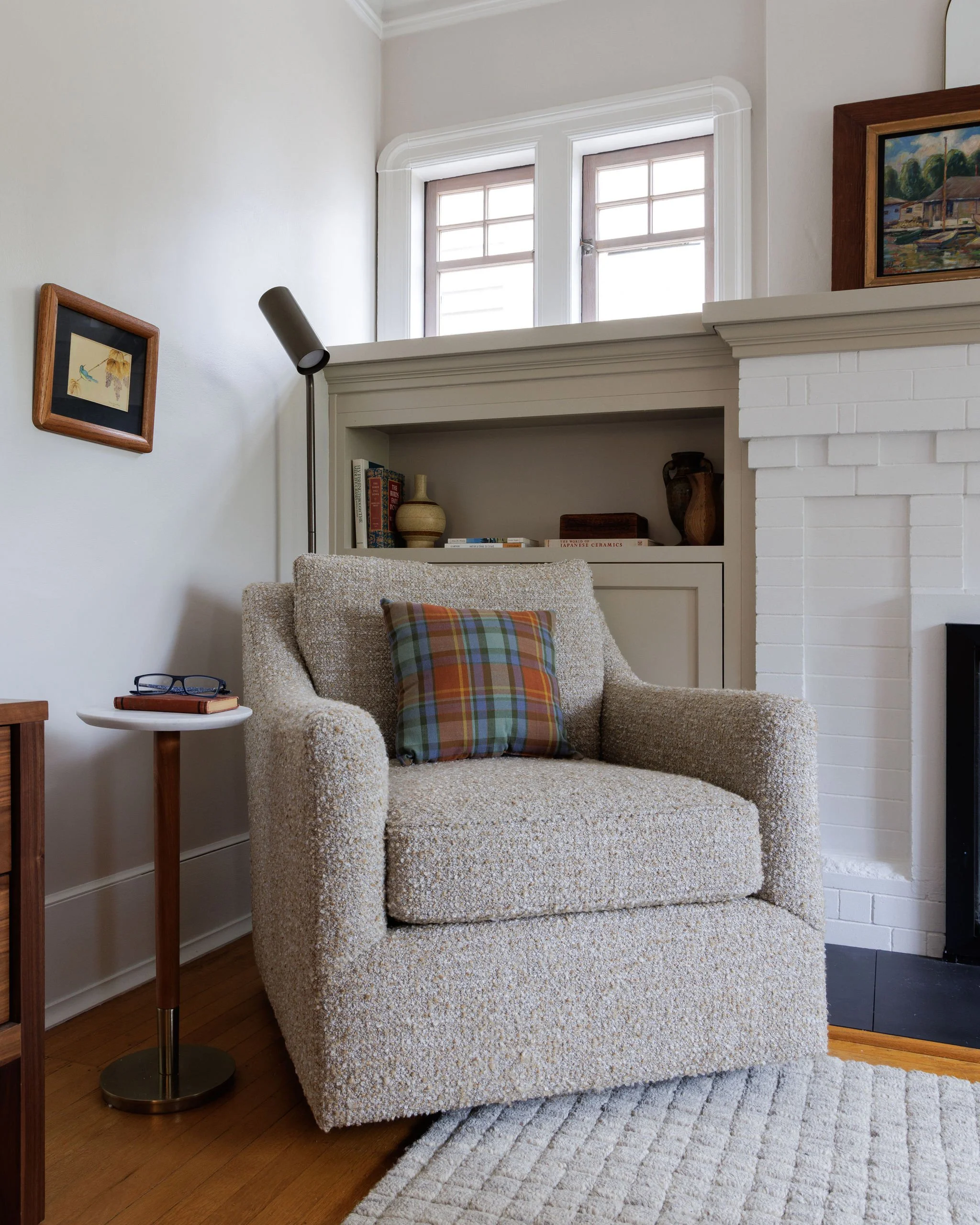 A transitional living room with a beige armchair and a side table next to a white brick fireplace with custom built-in shelves by Full Bloom Interior Design in Seattle.
