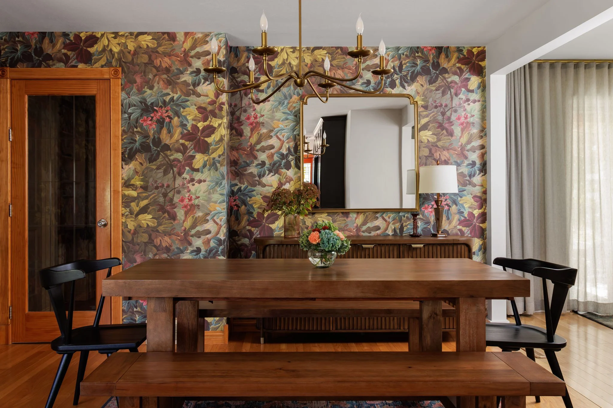 Eclectic dining room with a large walnut table, bench, black spindle chairs and bold floral wallpaper by Full Bloom Interior Design in Seattle.