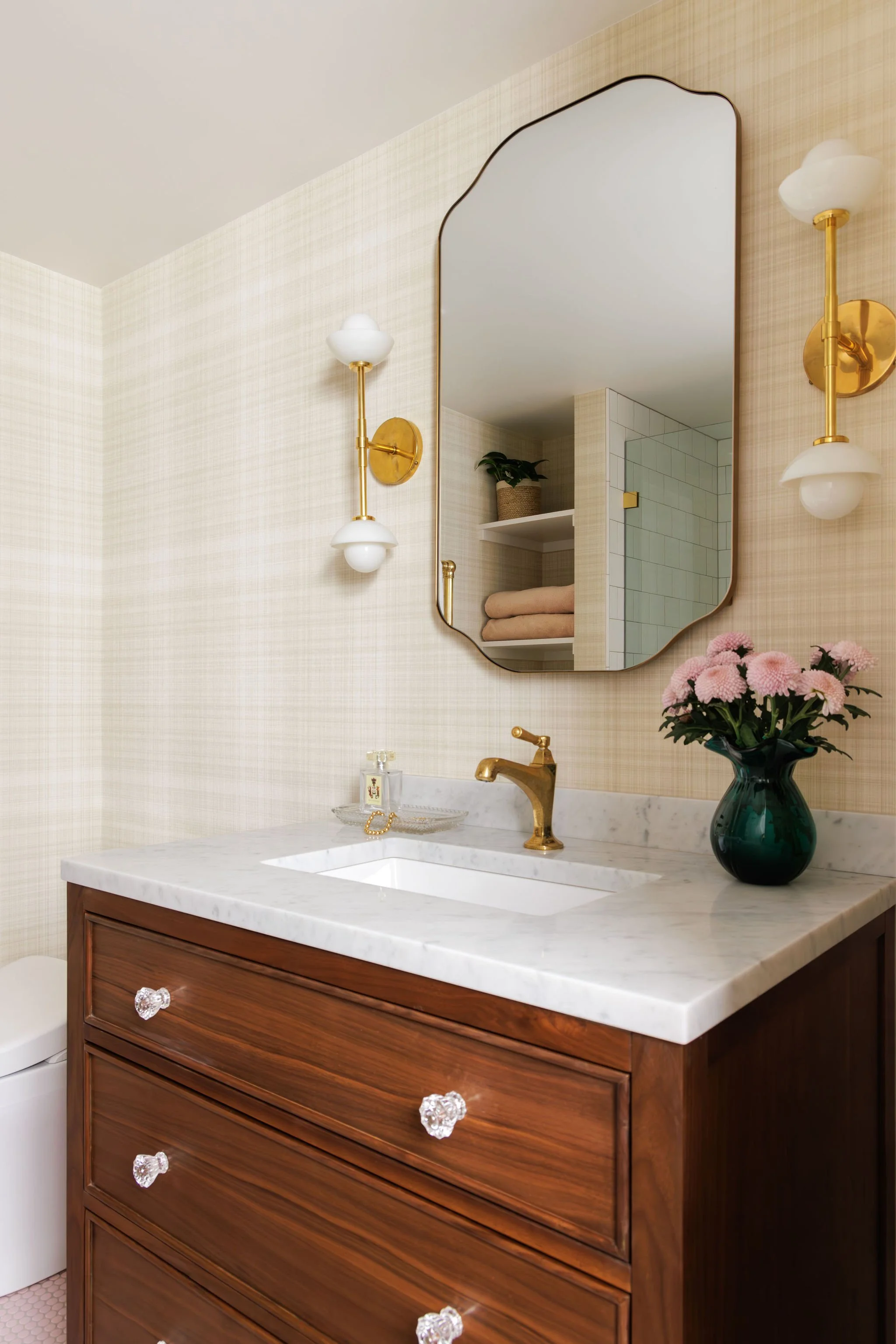 Traditional bathroom featuring a custom walnut vanity with glass knobs, a marble countertop, an elegant mirror, and gold sconces by Full Bloom Interior Design in Seattle.