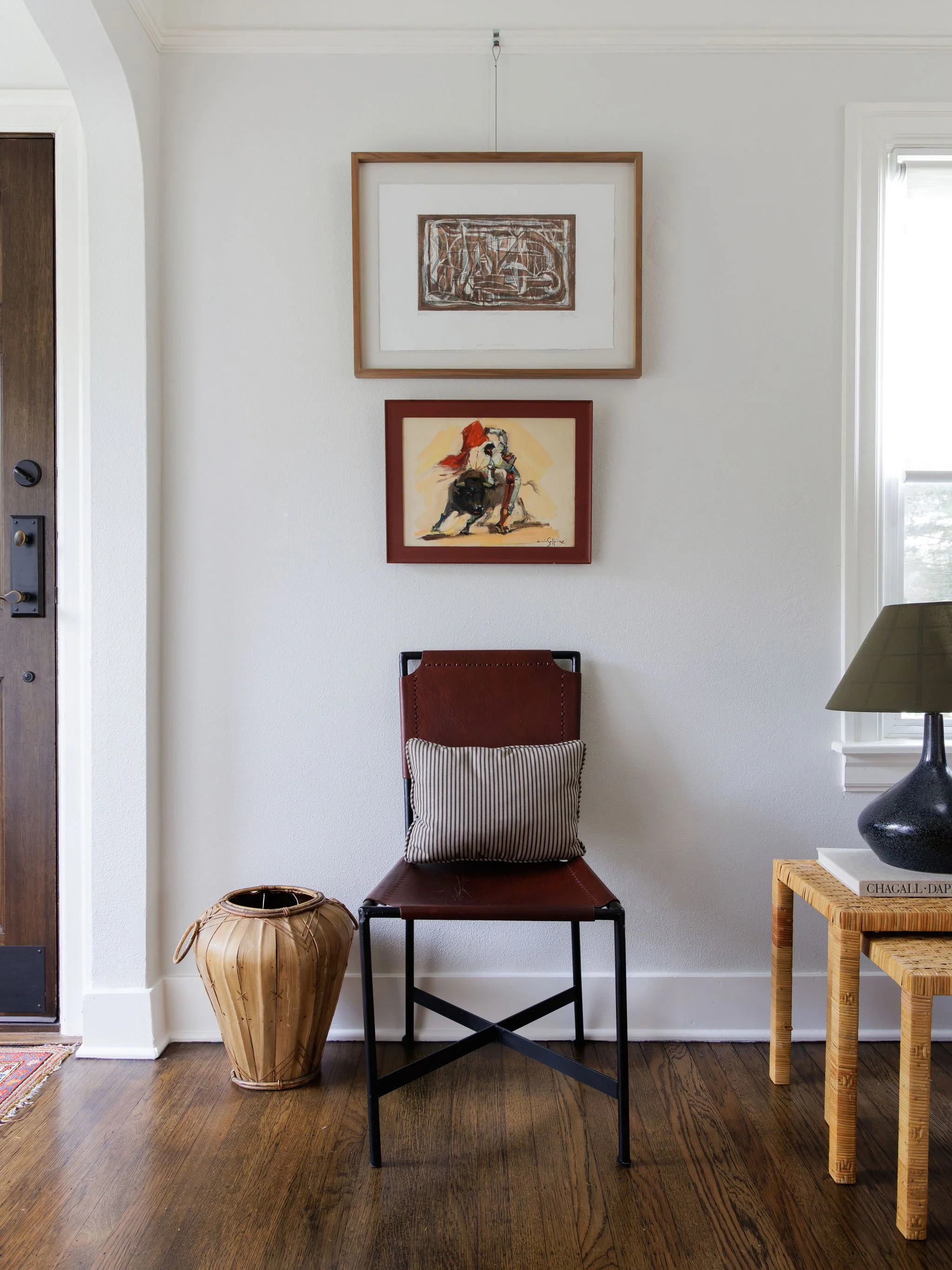 Seattle interior design entryway with leather accent chair, layered artwork, woven side table, and warm wood floors by Full Bloom Interior Design.