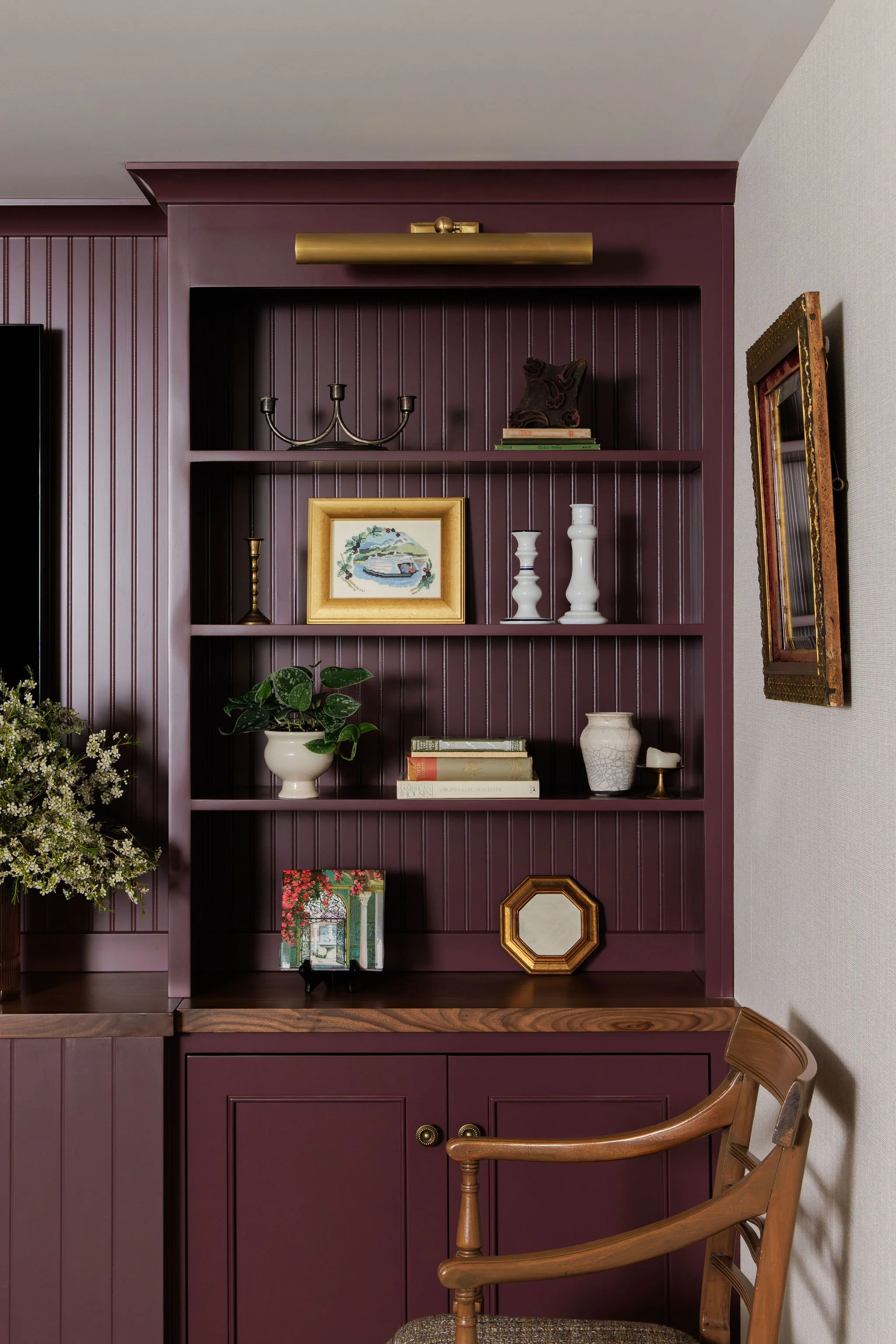 Detail of plum built-in bookshelves with a brass picture light, curated vintage decor and greenery by Full Bloom Interior Design in Seattle.