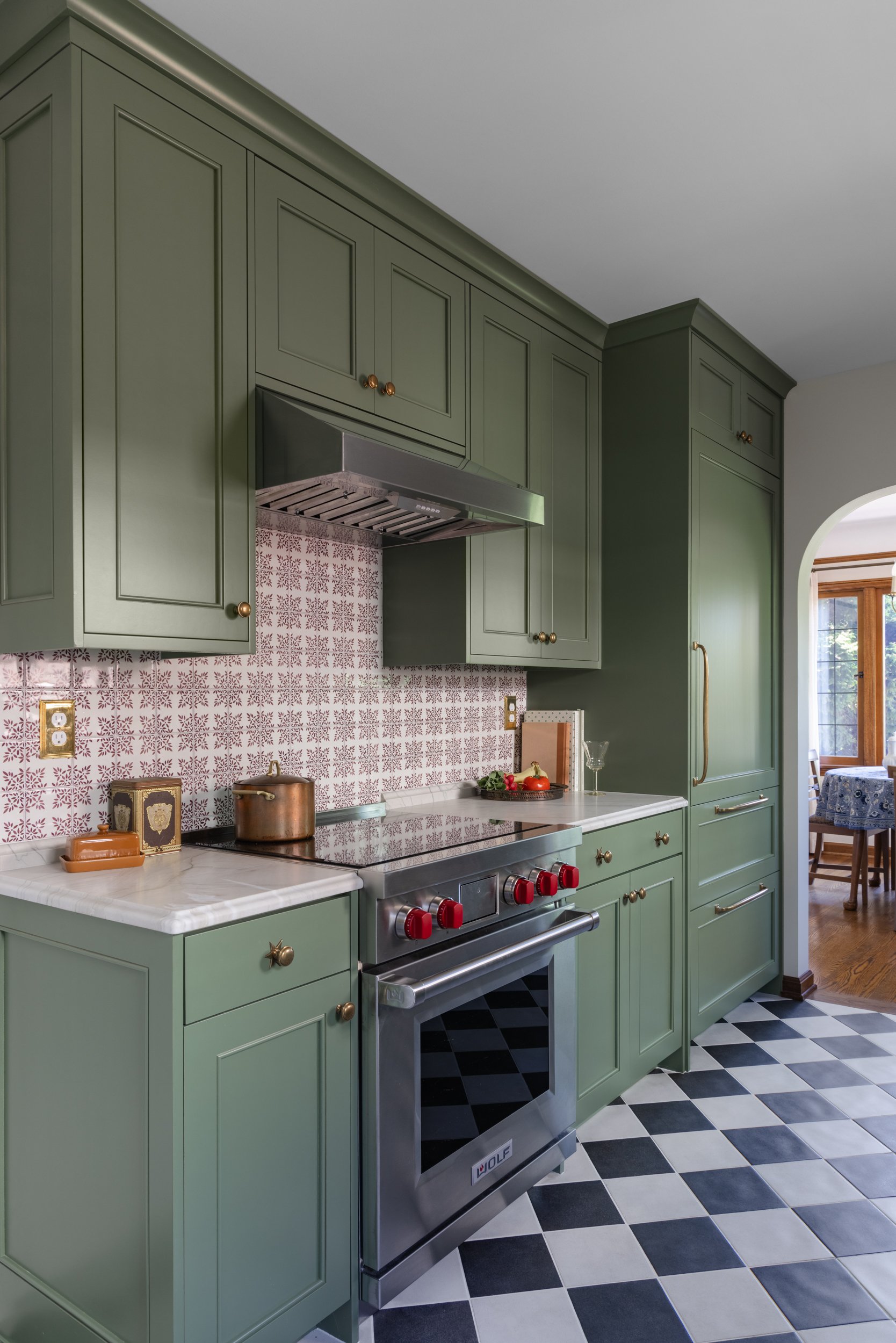 Kitchen featuring muted green cabinetry, black-and-white checkerboard flooring, a patterned tile backsplash, oven range, and marble countertops by Full Bloom Interior Design in Seattle.
