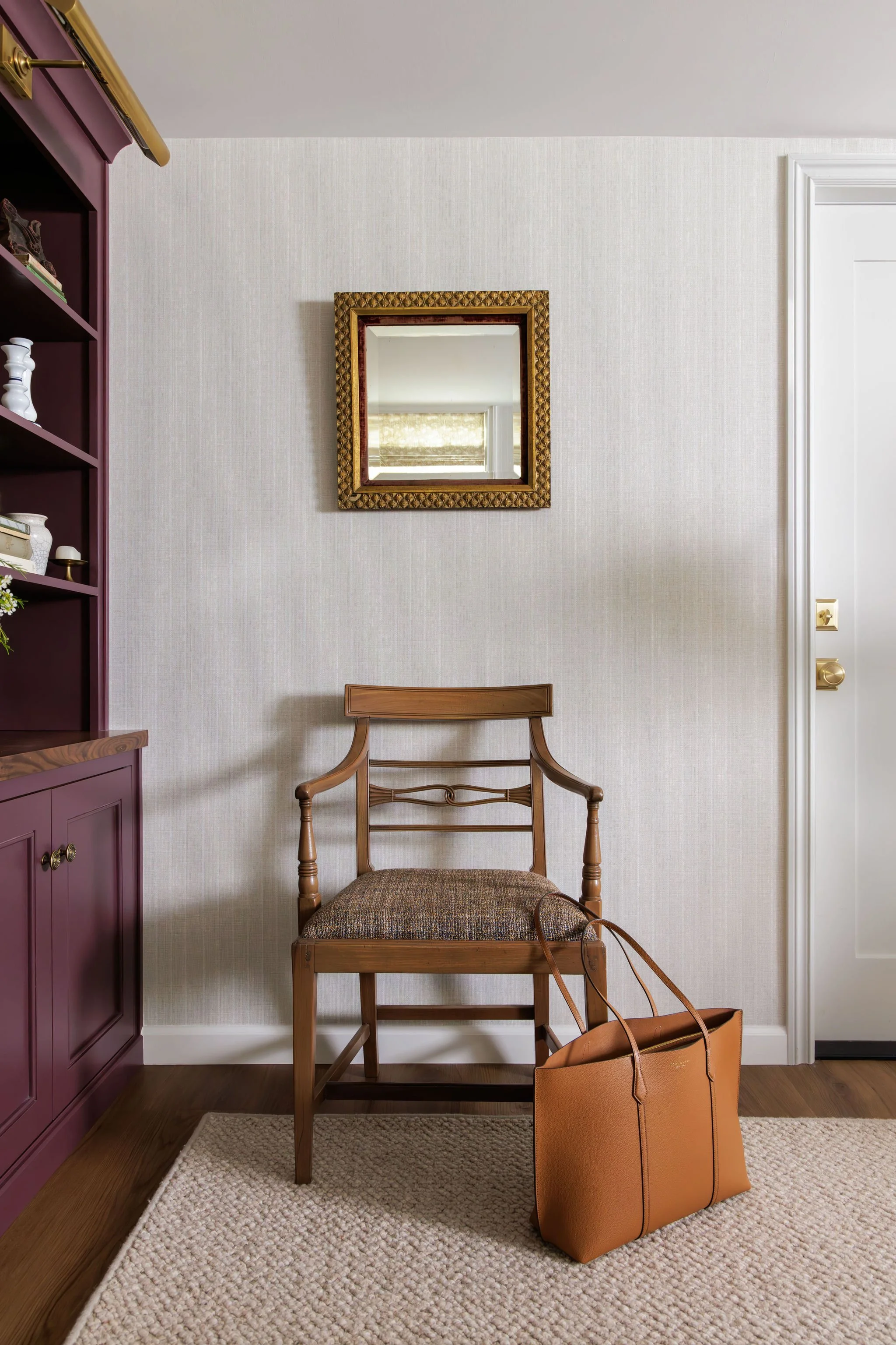 Basement remodel featuring a vintage wood armchair and a small gold-framed mirror against neutral textured wallpaper by Full Bloom Interior Design in Seattle.