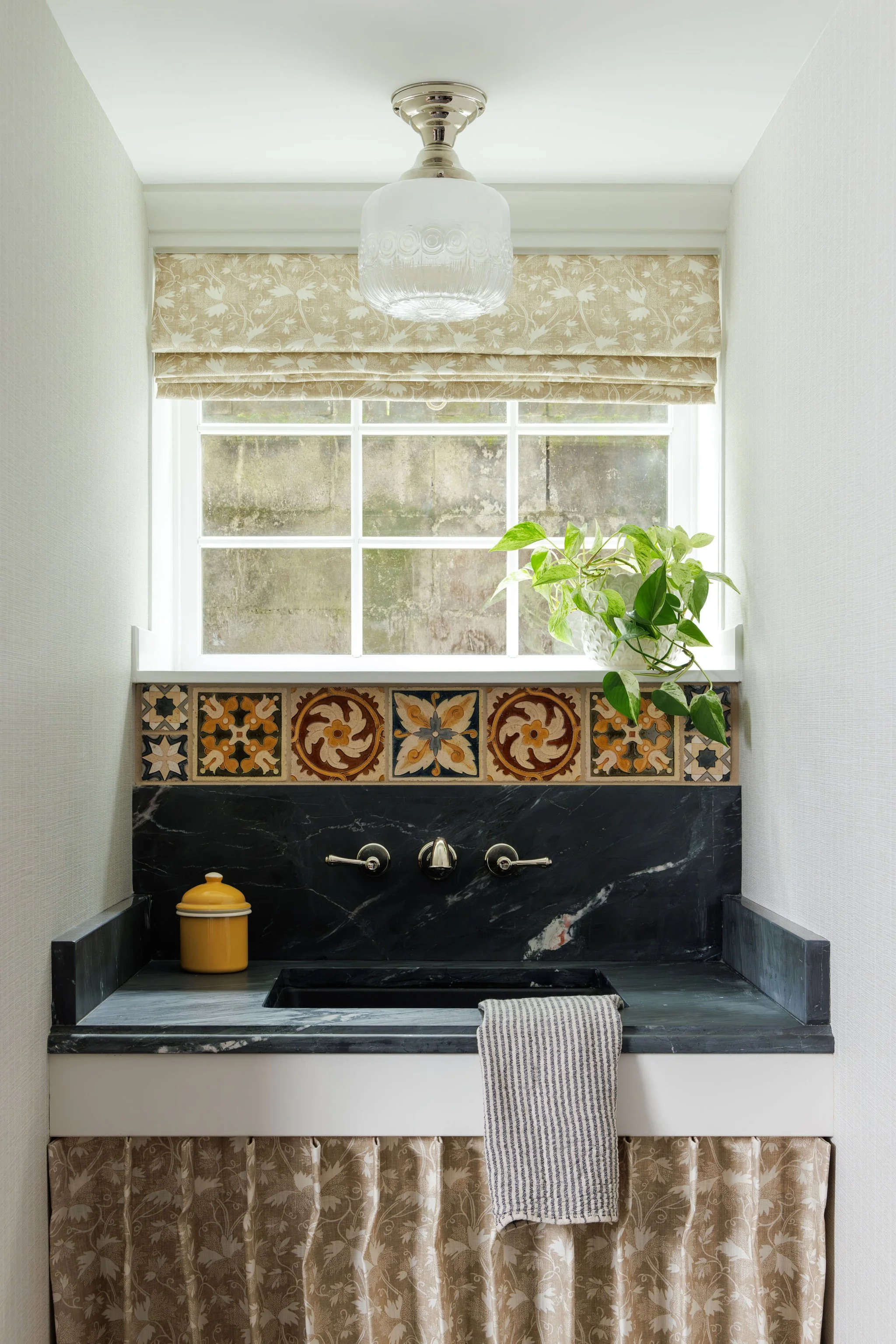 Custom laundry room featuring a soapstone counter, wall-mounted faucet, and decorative Portuguese tile backsplash by Full Bloom Interior Design in Seattle.