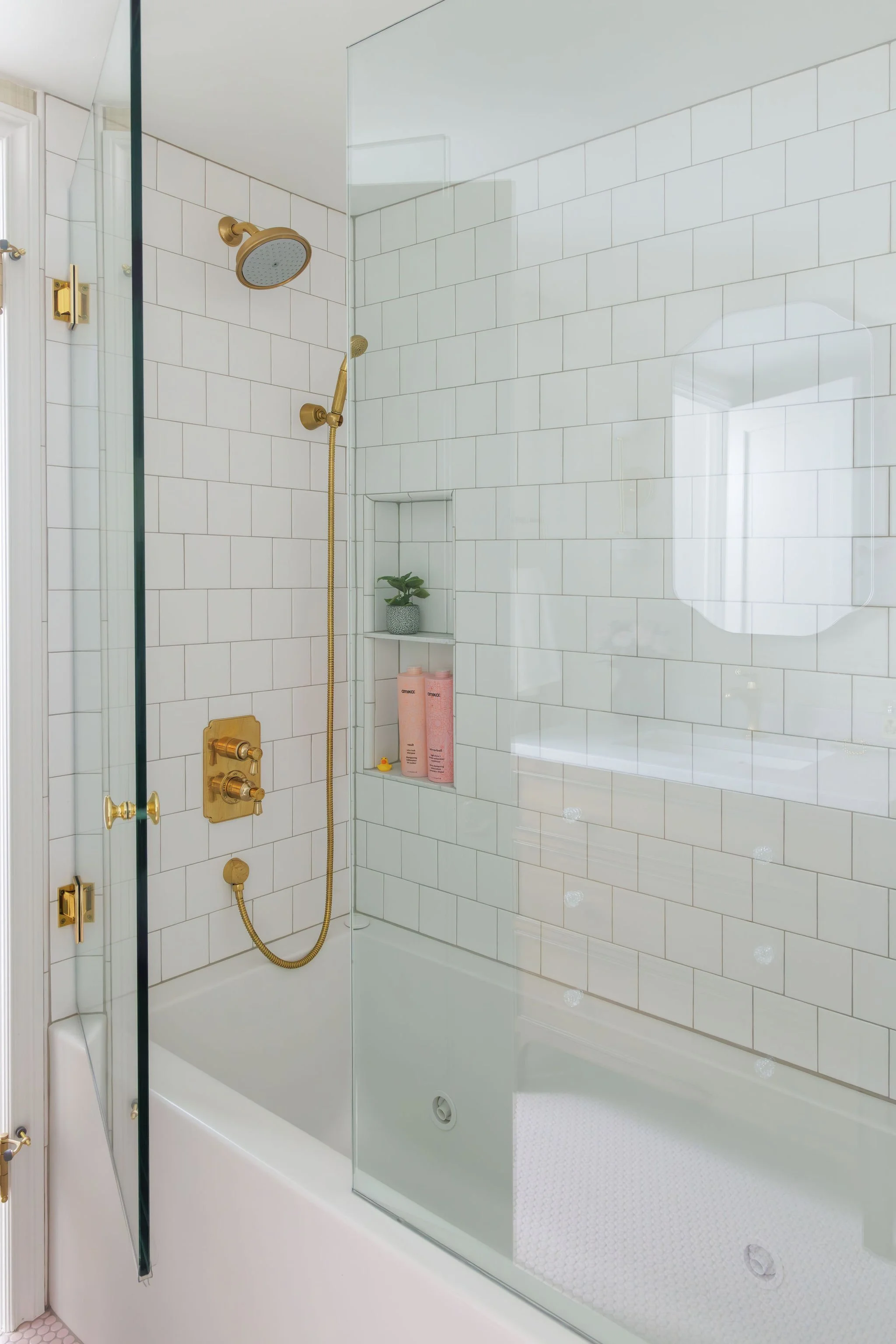 Bright shower and tub with white subway tile and aged brass fixtures by Full Bloom Interior Design.
