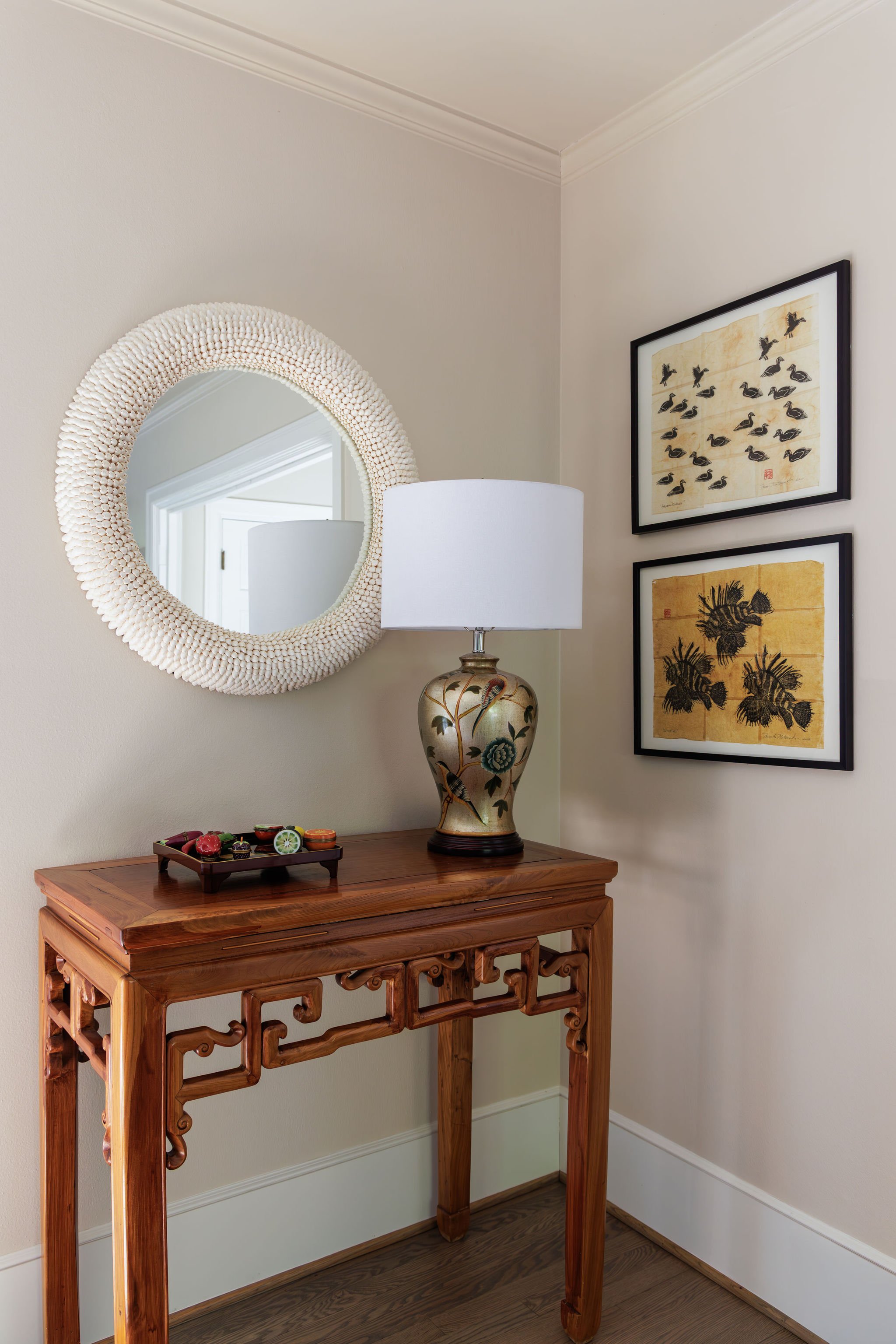 A carved wooden console table, white circular mirror, vintage-style lamp, decor and wall art by Full Bloom Interior Design in Seattle.