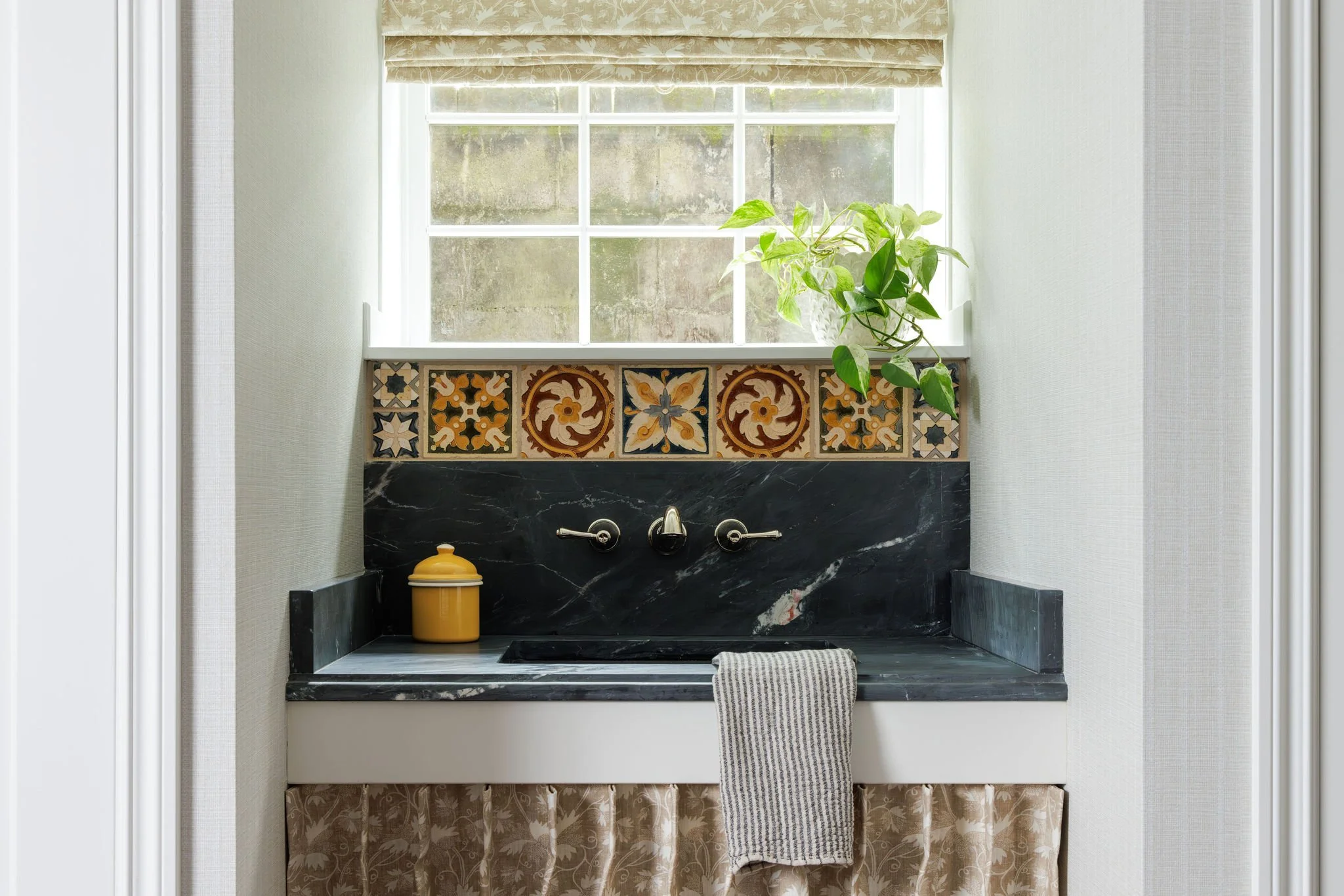Close-up of a soapstone utility sink with a wall-mounted faucet, Portuguese tile and botanical roman shade by Full Bloom Interior Design in Seattle.