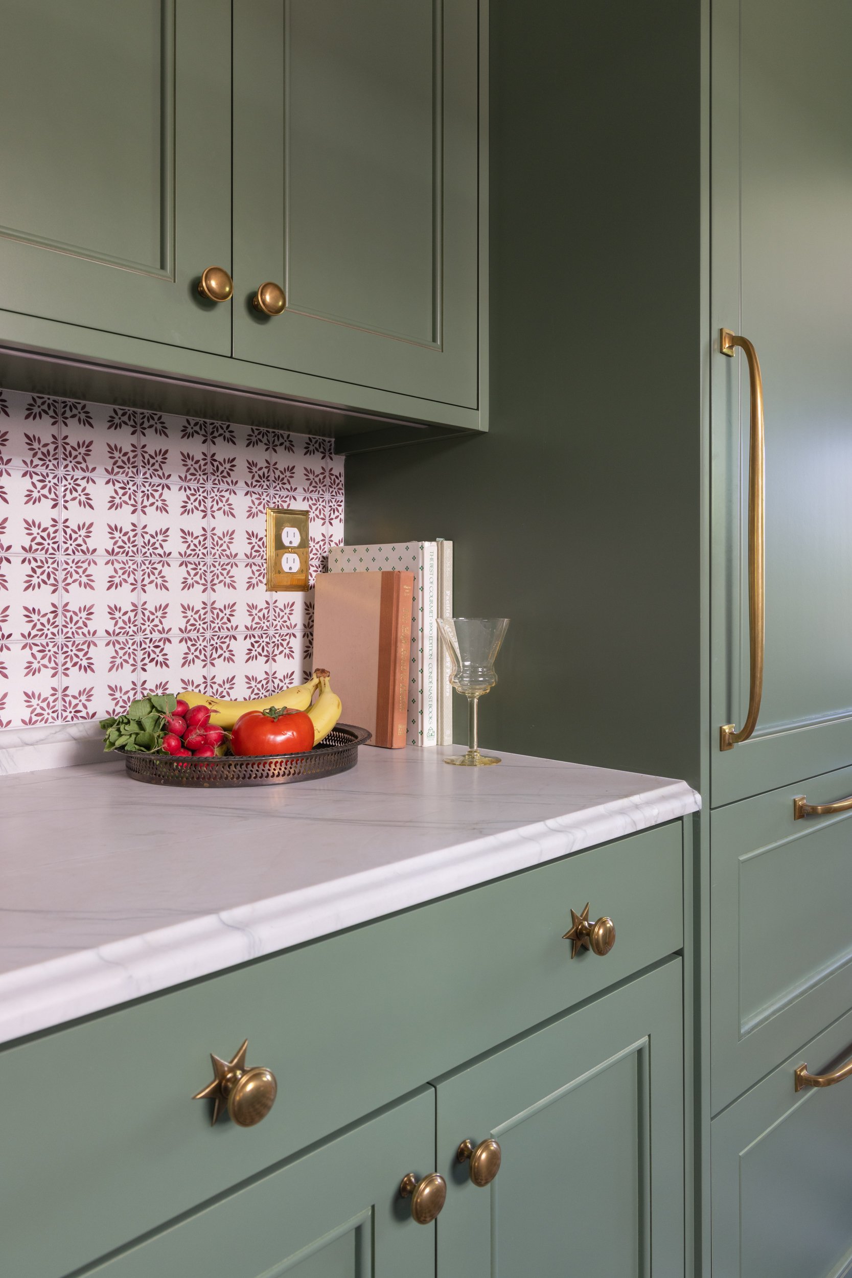 Detailed view of muted green cabinetry, marble countertops, patterned tile backsplash, and brass hardware by Full Bloom Interior Design in Seattle.