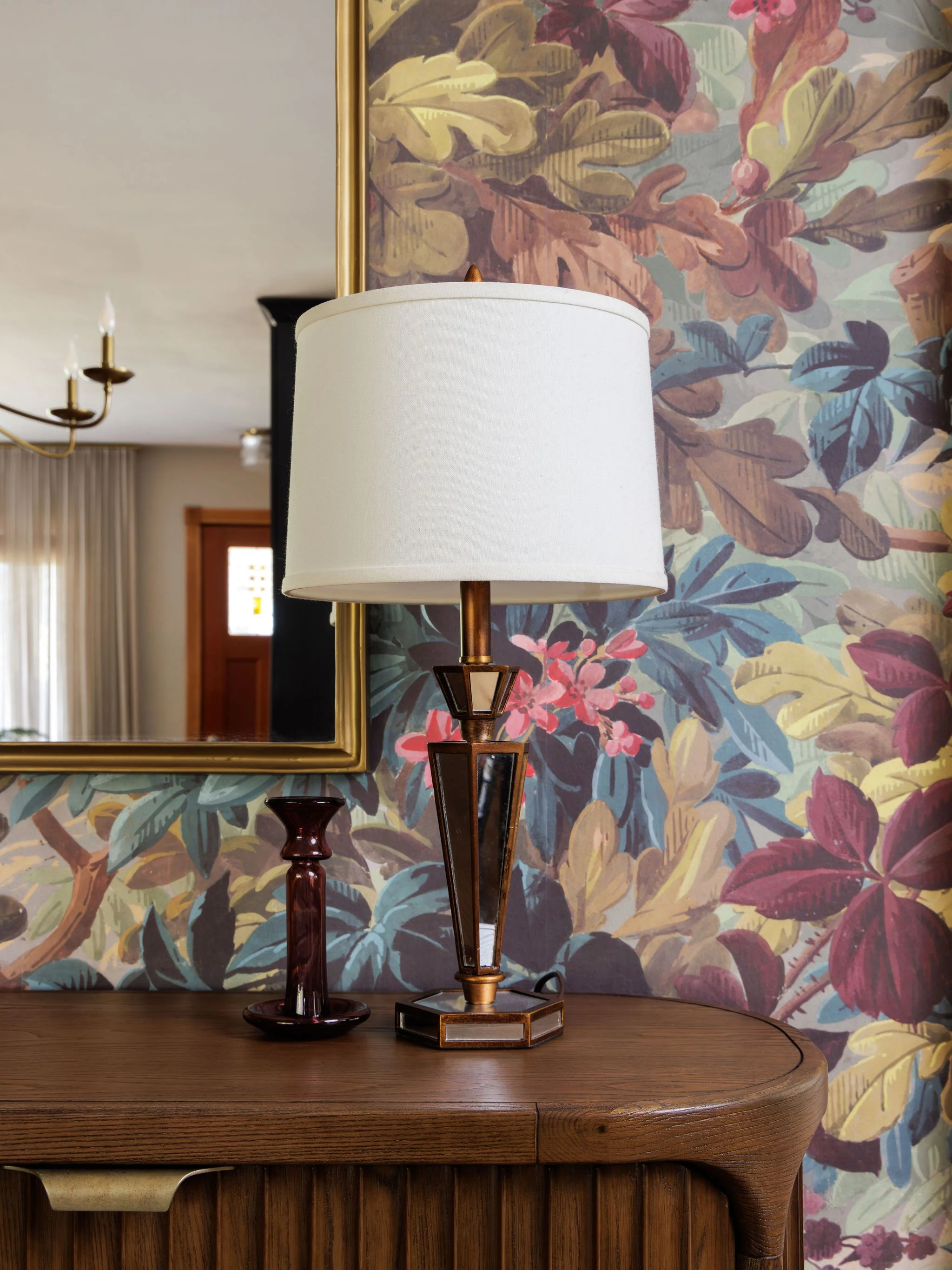 Mid-century fluted wood sideboard styled with a gold mirror, Art Deco lamp and candlestick, set against vibrant floral wallpaper by Full Bloom Interior Design in Seattle.