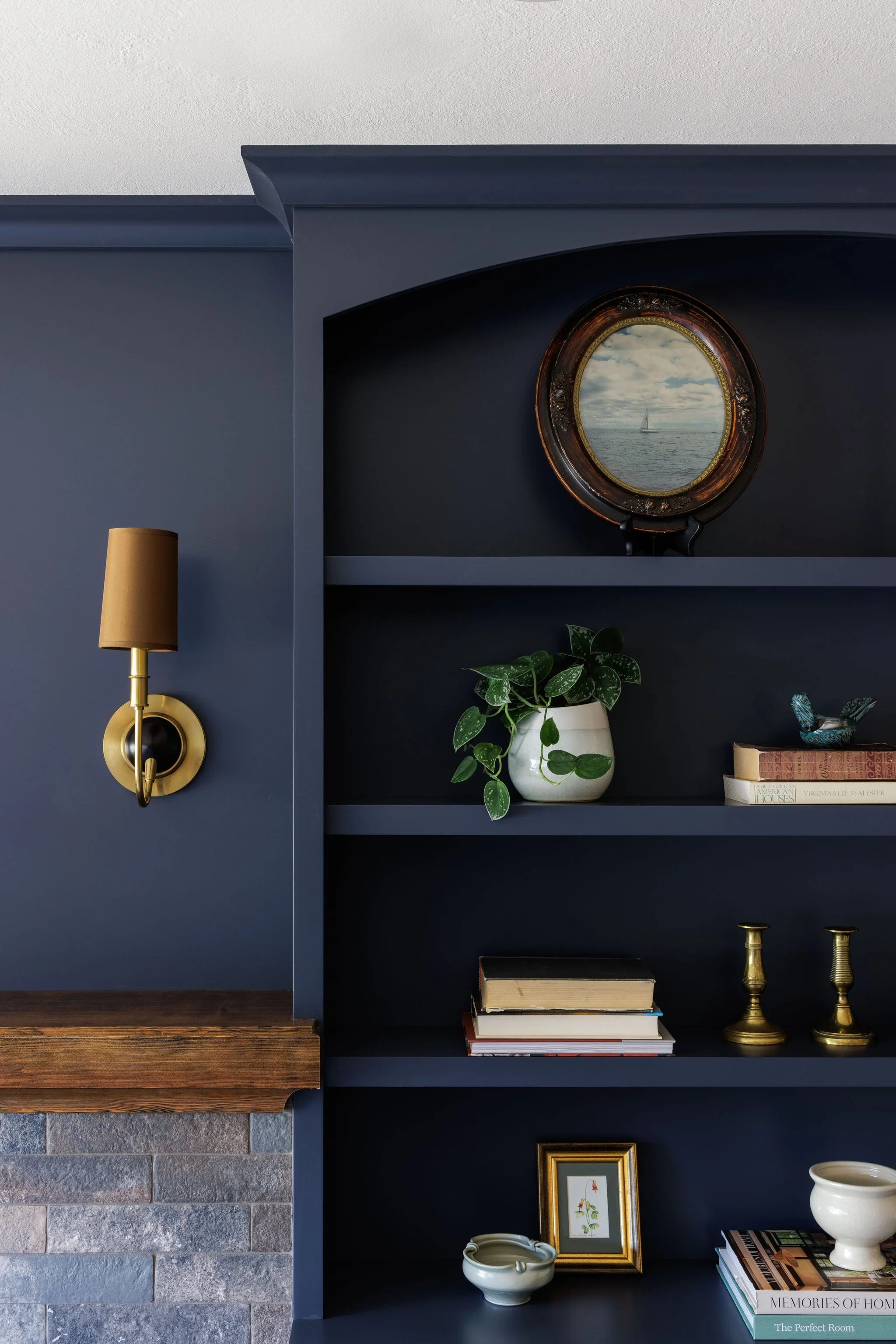 Custom navy blue built-in bookshelves styled with vintage art, brass candles, books, greenery and decor by Full Bloom Interior Design in Seattle.