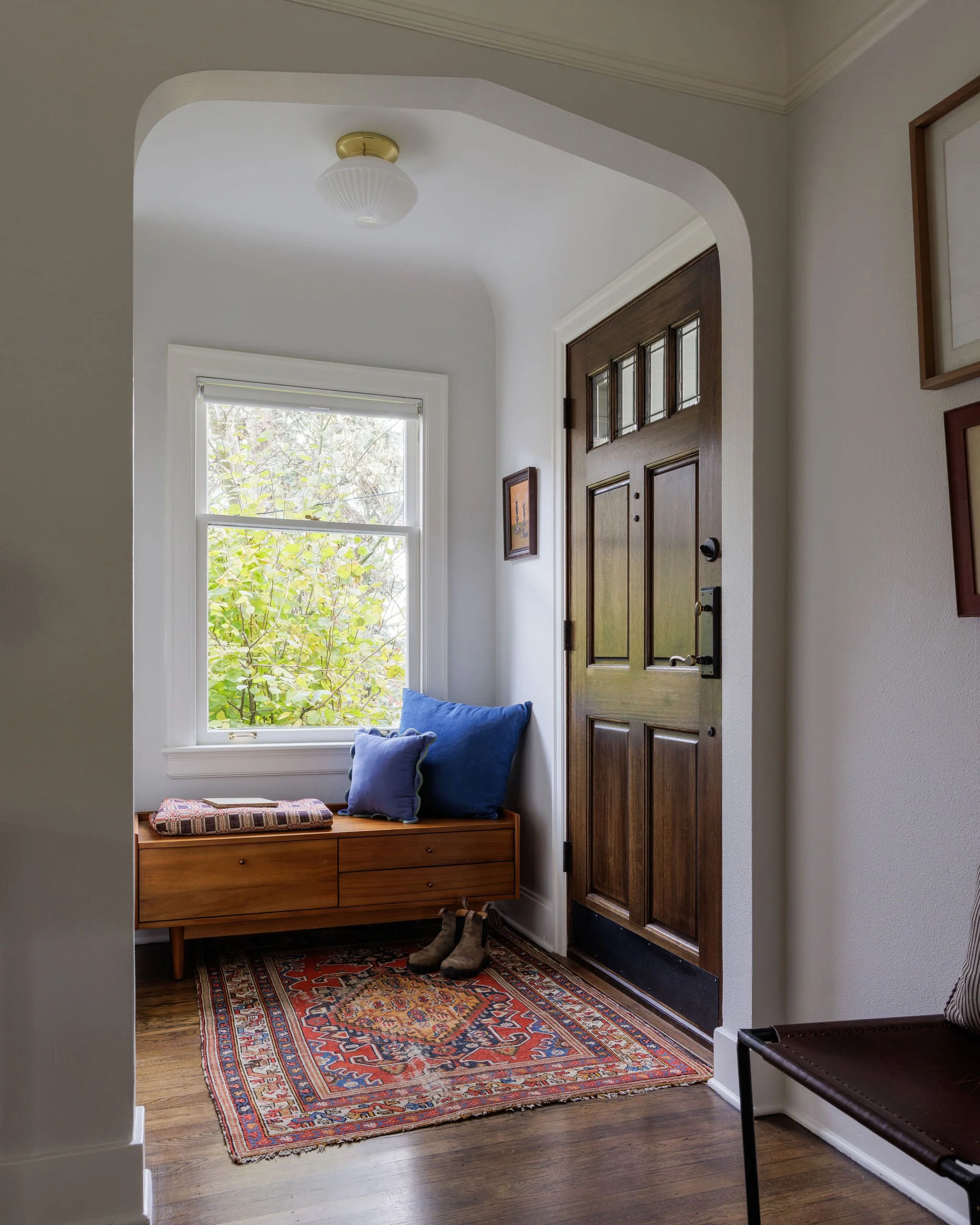 Tudor entryway design in Seattle featuring a mid-century modern bench with a folded quilt and pillows, a vintage rug, and an architectural archway.
