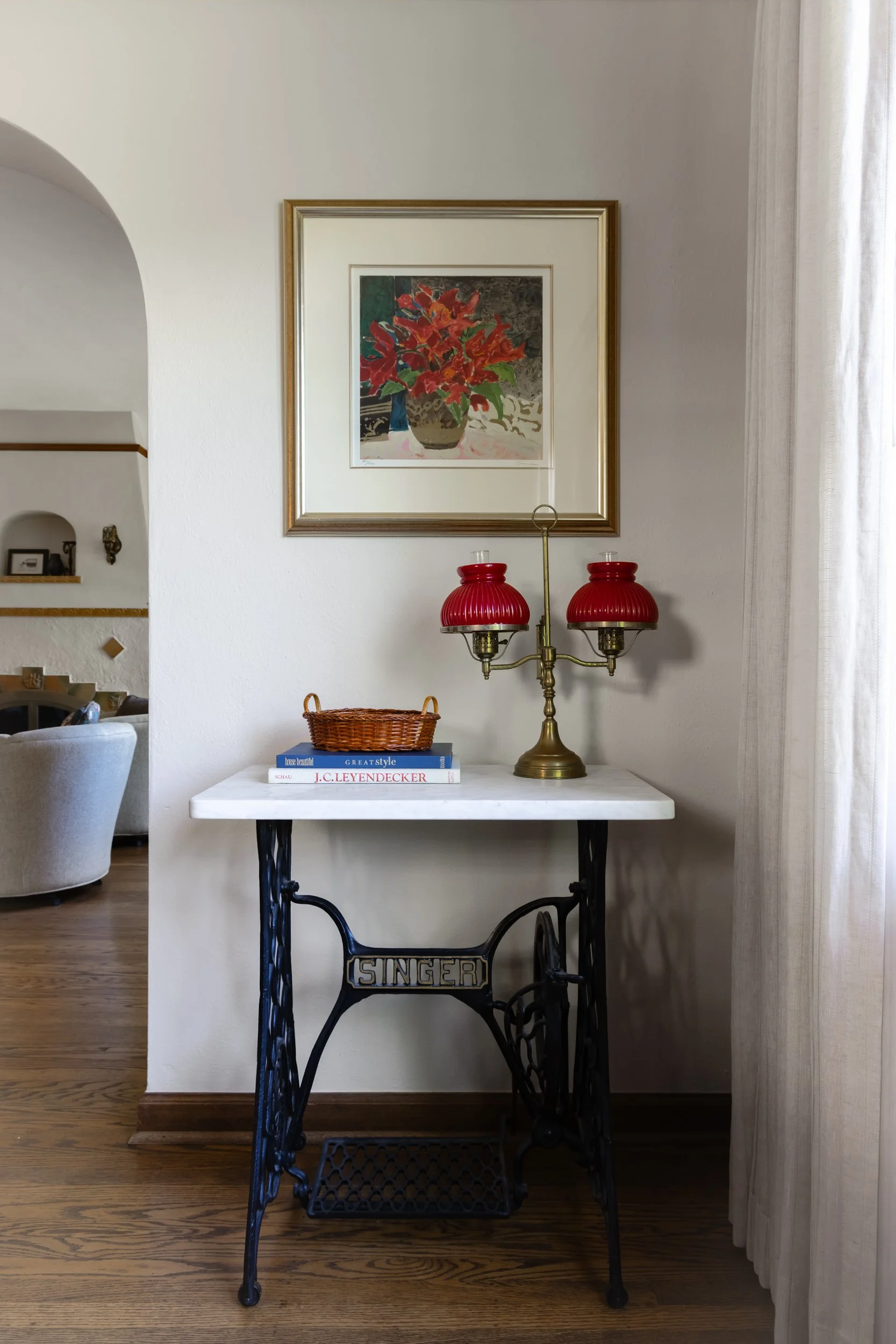 Detailed vignette featuring a vintage Singer sewing machine table with a marble top, red glass lamp, and framed artwork by Full Bloom Interior Design in Seattle.