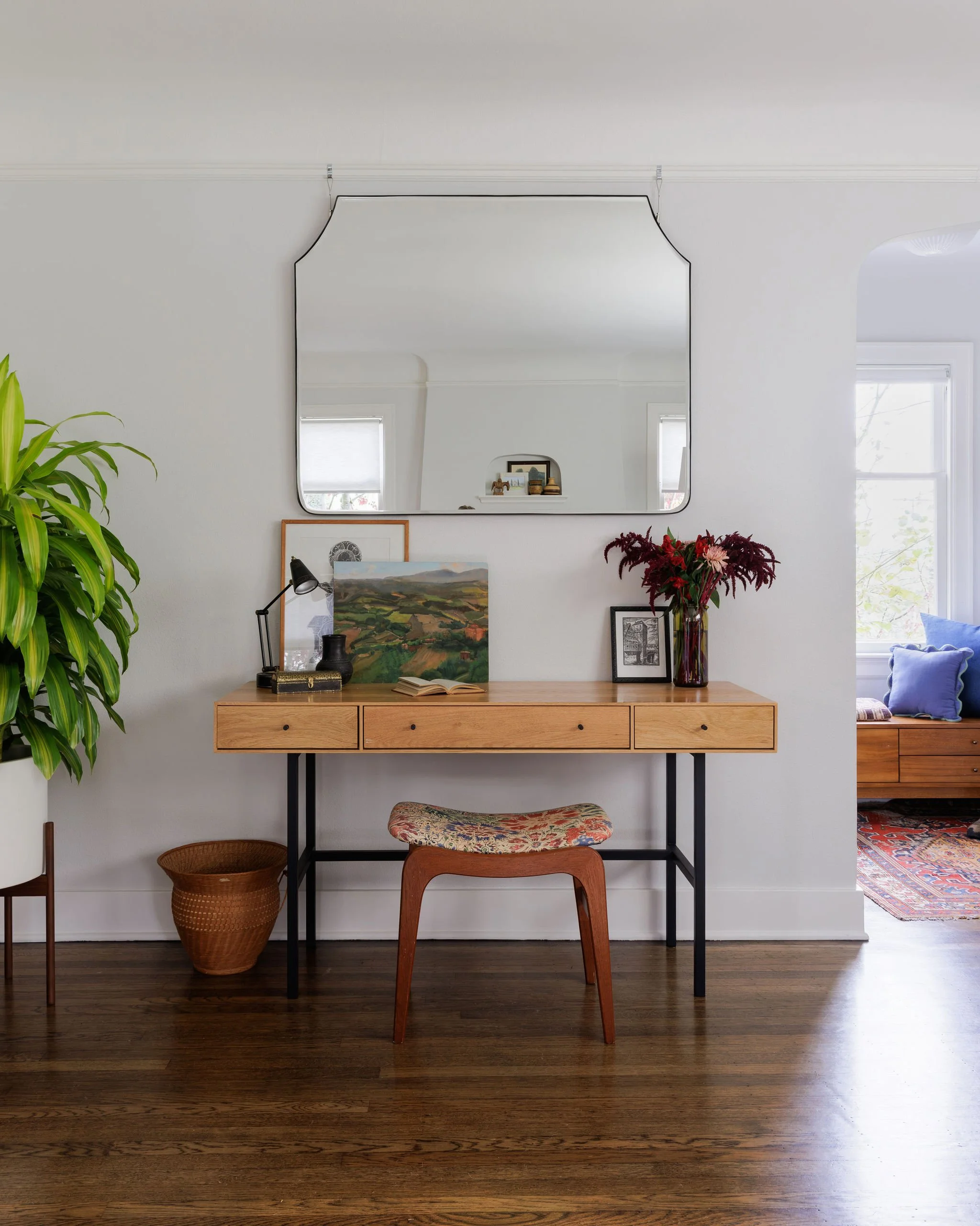 Mid-century modern wood desk with a vintage floral stool and large silver wall mirror in a curated Tudor living room by Full Bloom Interior Design in Seattle.