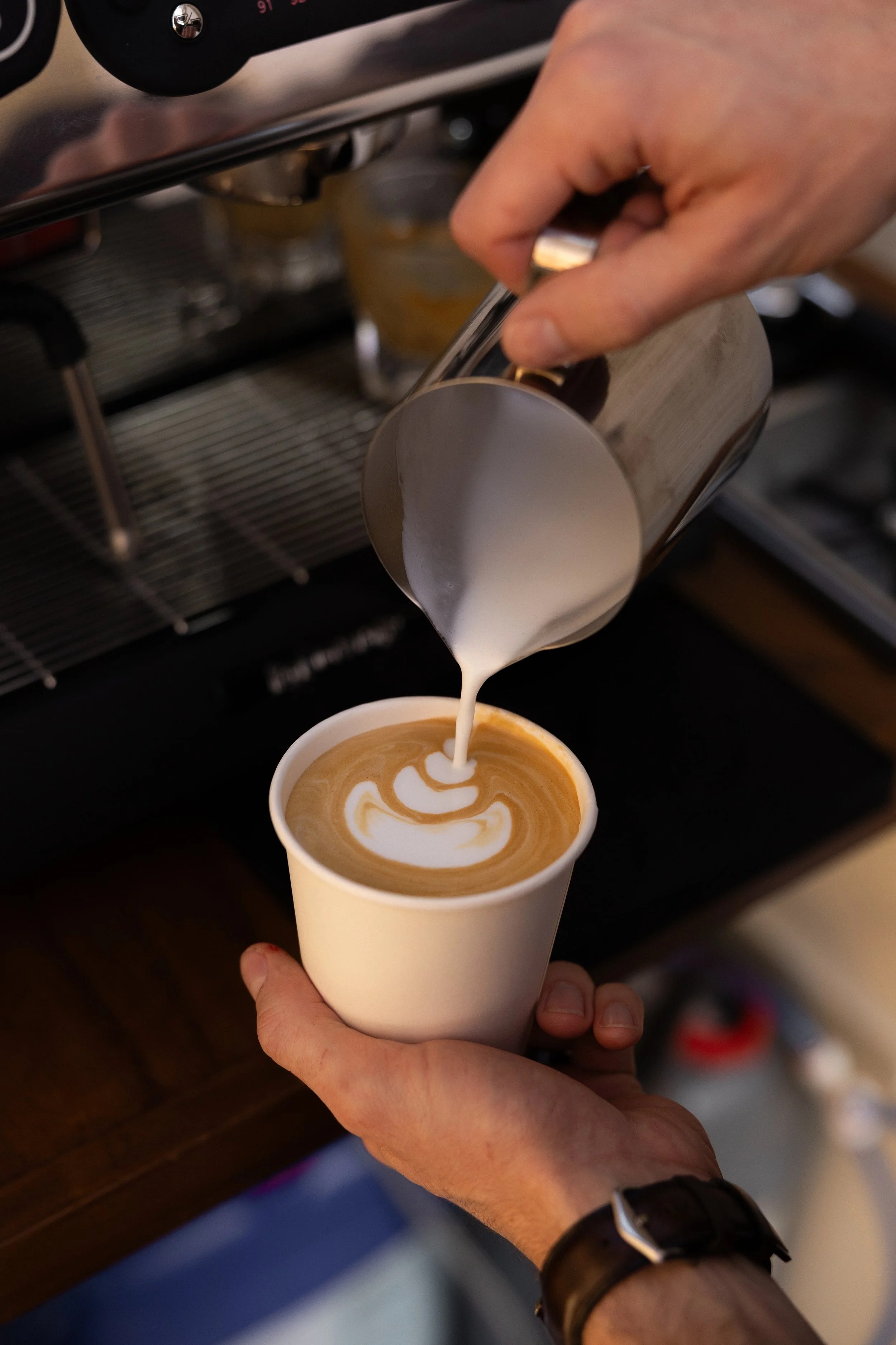 A barista pours steamed milk creating latte art in a cup of coffee.