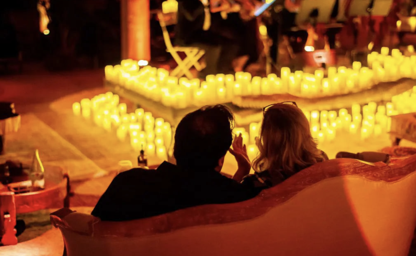 Couple sitting on a sofa at night, engaged in conversation, with numerous candles illuminating the background.